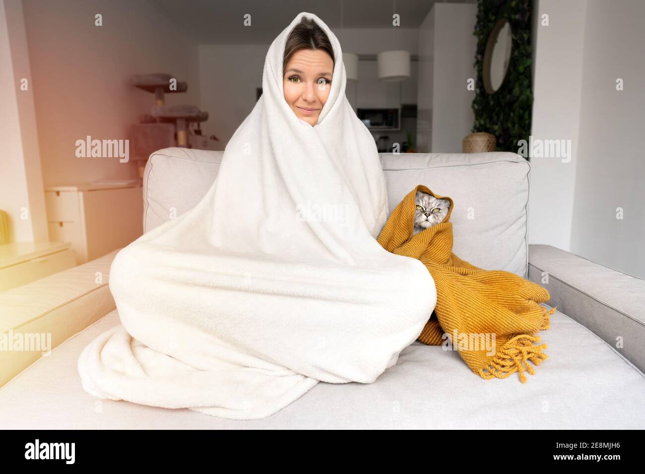 Frau, die sich kalt fühlt. Frau und Katze wärmen sich unter einer Decke auf dem Sofa zu Hause. Frost vor Kälte Stockfoto