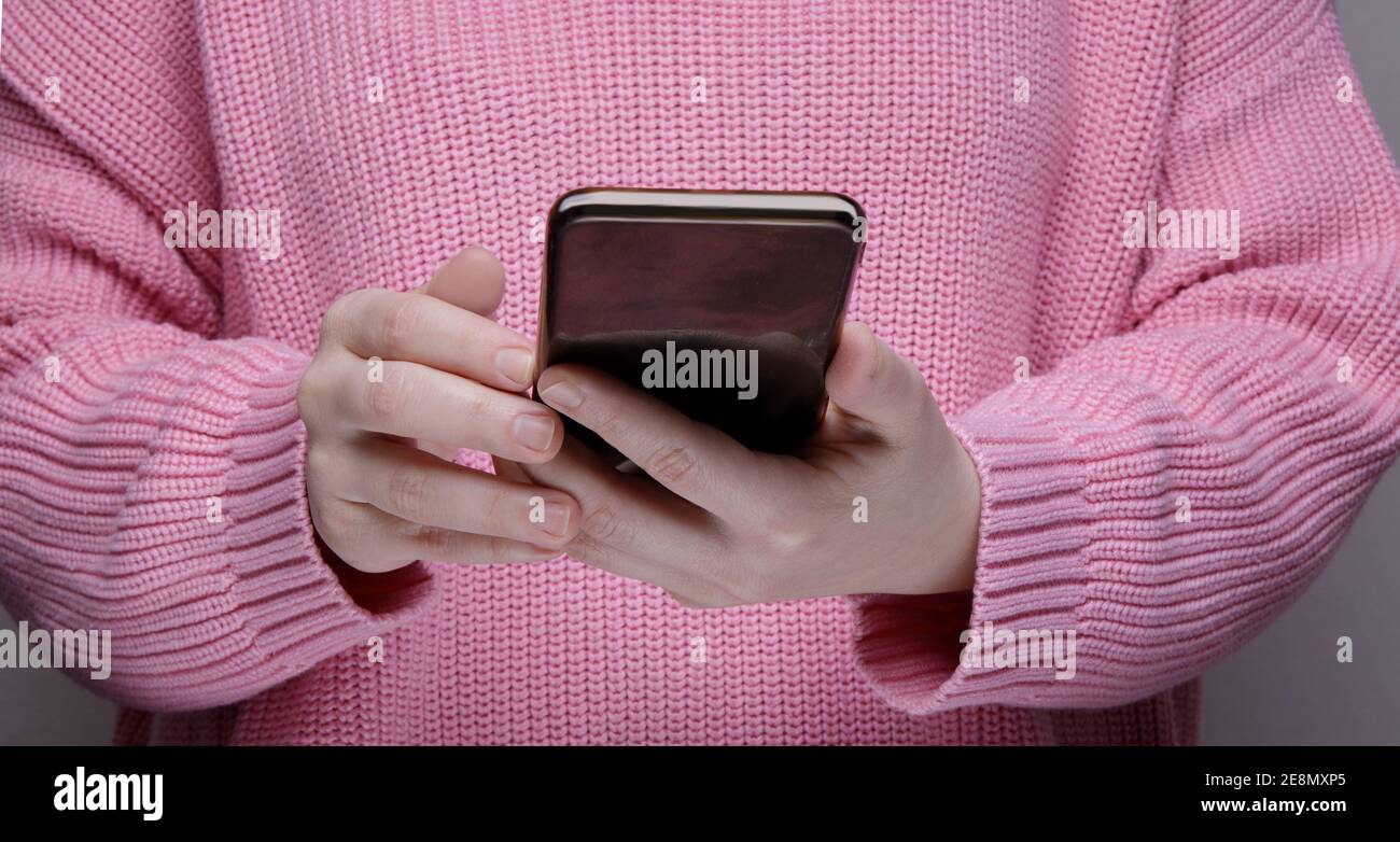 Hände ein Mädchen in einem rosa Pullover hält einen schwarzen Smartphone Stockfoto