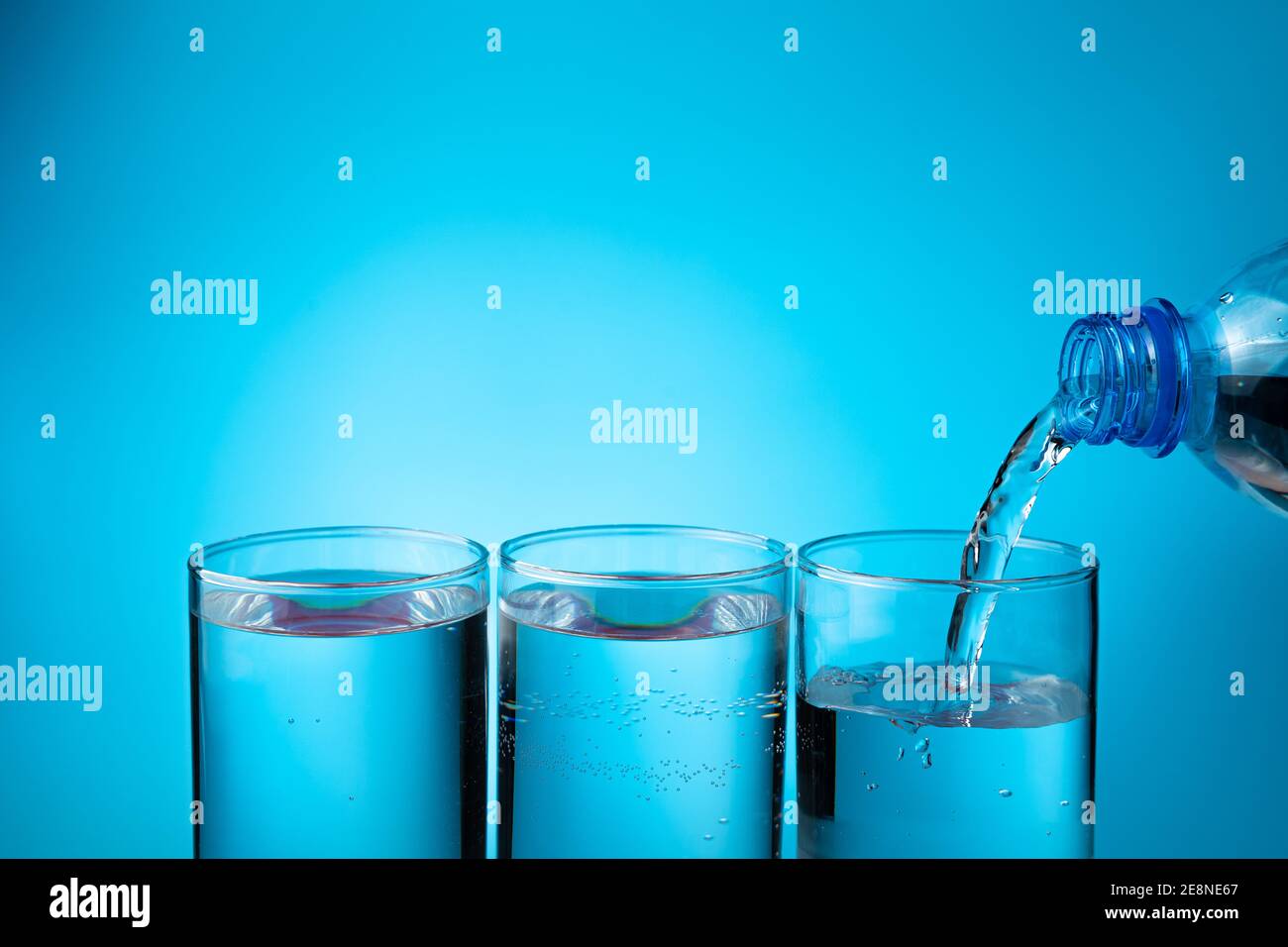 Wasser in Gläsern, drei Gläser aus einer Plastikflasche auf blauem Grund füllend. Stockfoto