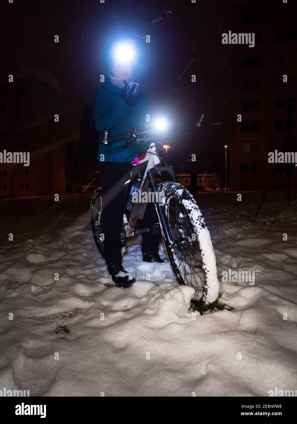 Teenager Junge mit mtb im Winter verschneiten Park. Kind halten Telefon und sitzen auf einem Fahrrad. Boy mit blau schwarz warmer Tragevariante, Helm und leuchtendem Scheinwerfer. Stockfoto