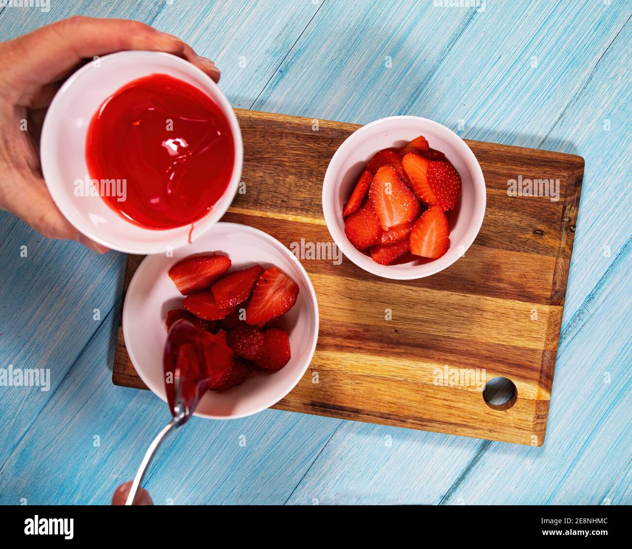 Erdbeeren in Scheiben geschnitten in weißen Schüsseln mit Mann hinzufügen Fruchtglasur zu ihnen. Stockfoto