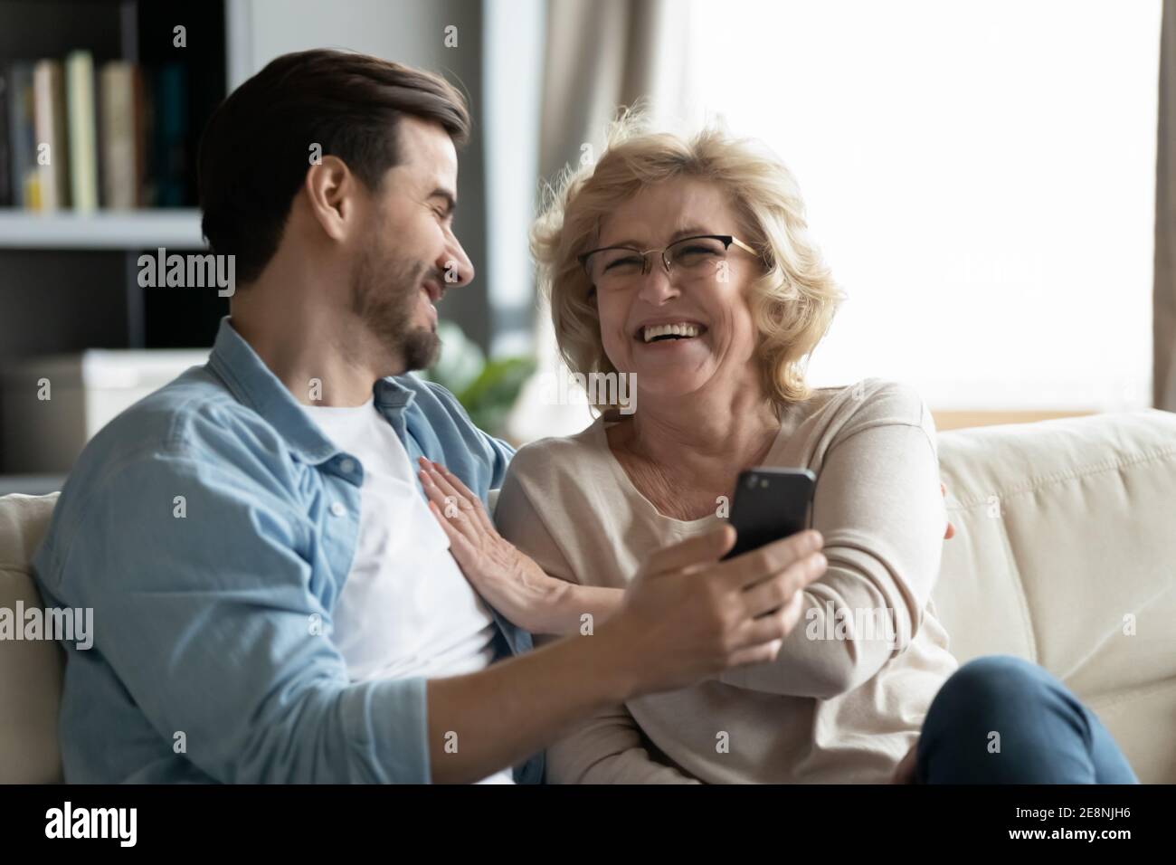 Junger Mann zeigt lustige Fotos auf dem Smartphone zu reifen Mutter. Stockfoto