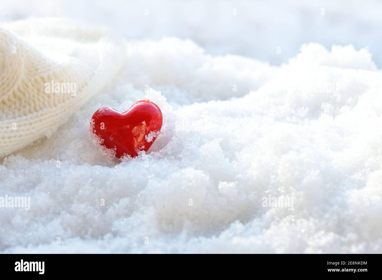 Rote Herzform aus Glas neben einem Wollschal im weißen Schnee, Liebessymbol und Winterurlaubskonzept, Kopierraum, ausgewählter Fokus, schmal de Stockfoto