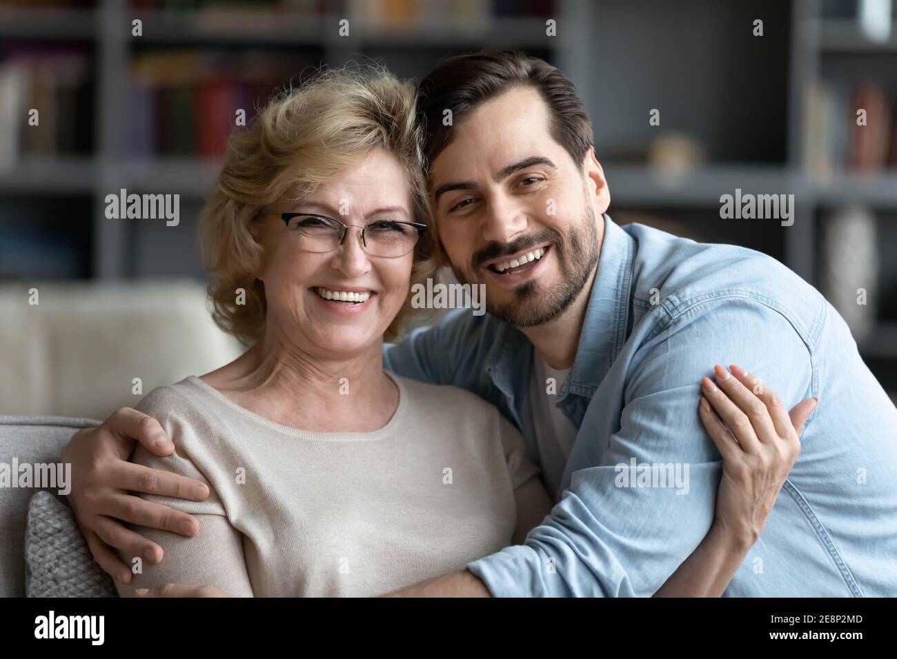 Porträt eines lächelnden jungen Mannes, der die ältere Mutter in einer Brille umarmt. Stockfoto