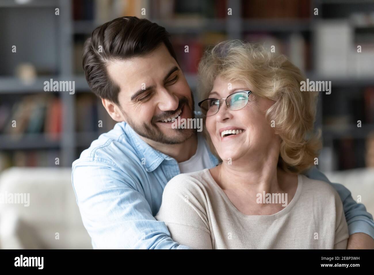 Glücklicher junger Mann umarmt ältere Mutter zu Hause. Stockfoto