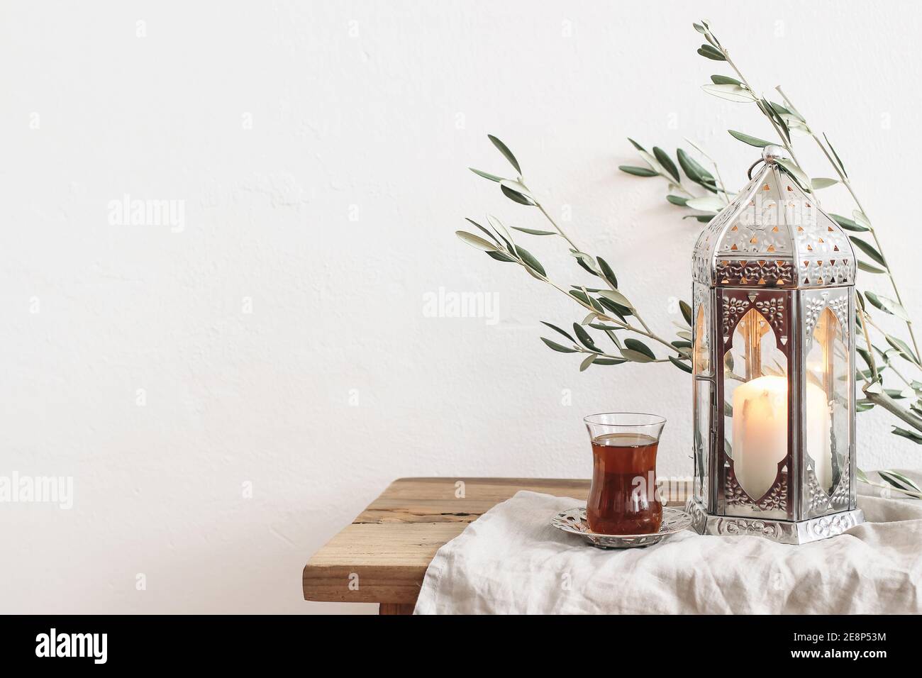 Ramadan Kareem Grußkarte, Einladung. Silberne Laterne mit brennender Kerze. Türkischer Tee im Glas auf Untertasse. Grüner Olivenbaum Äste auf altem Holz Stockfoto