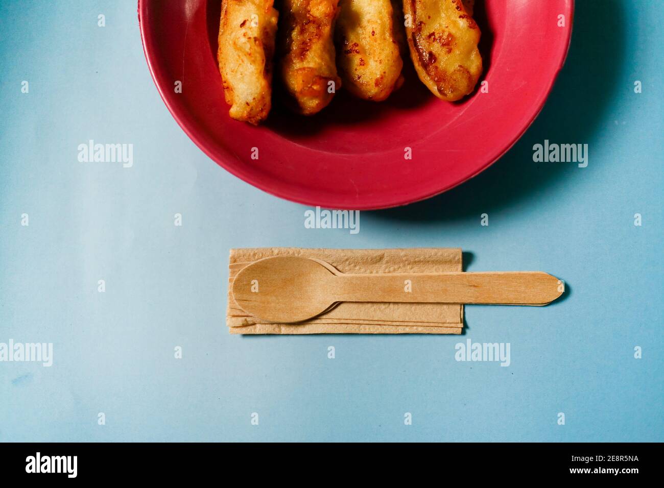 Banane gebraten auf rotem Teller mit Holzgerät isoliert auf Blauer Hintergrund Stockfoto