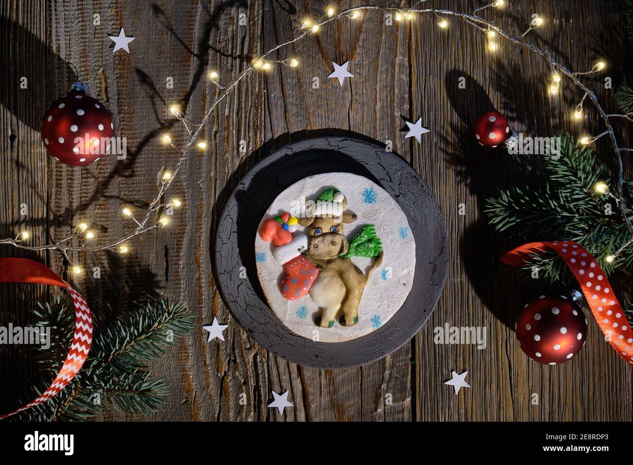 Verzierte Lebkuchen mit dummen lustige Kuh mit Weihnachten Socke voller Geschenke dekoriert. Weihnachtliche Wohnung mit Tannenzweigen, roten Kugeln und festlichen Lichtern Stockfoto