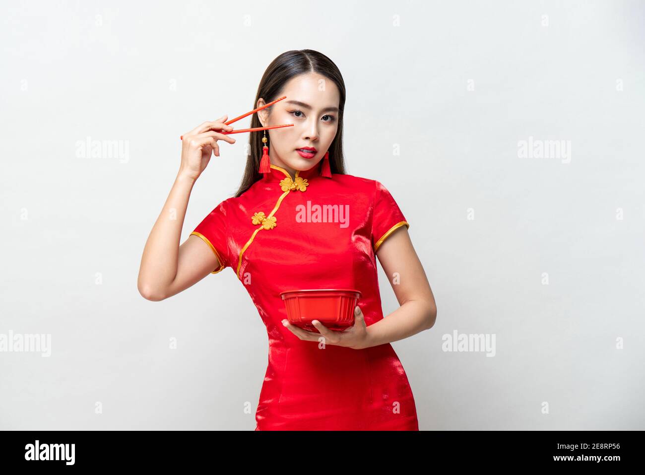 Schöne asiatische Frau in traditionellen roten chinesischen Qipao Kleid halten Lebensmittelbox und Essstäbchen in Studio isoliert grauen Hintergrund Stockfoto