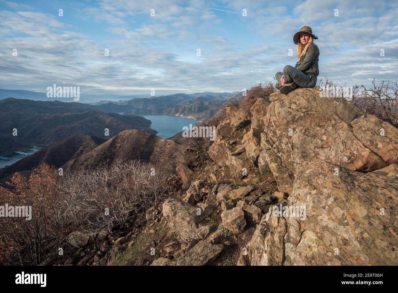 Eine Wanderin sitzt auf einigen Felsen mit Blick auf das Tal und den Stausee unten in der kalifornischen Wildnis. Stockfoto