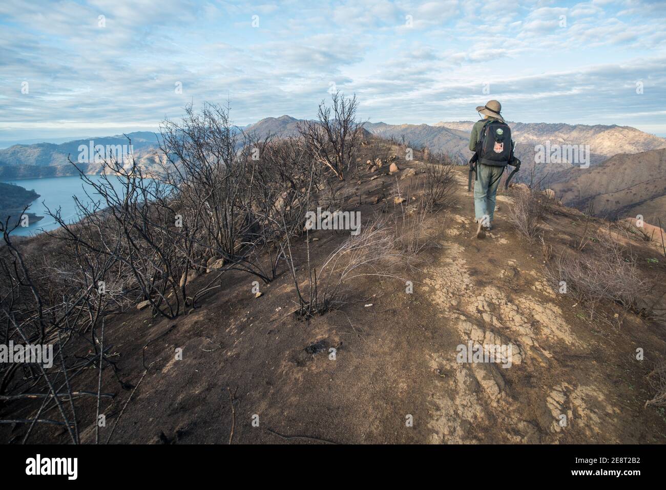 Ein Wanderer mit Blick weg und zu Fuß in die Ferne entlang der Kamm eines Hügels mit Blick auf einen See und Berge, in Kalifornien. Stockfoto