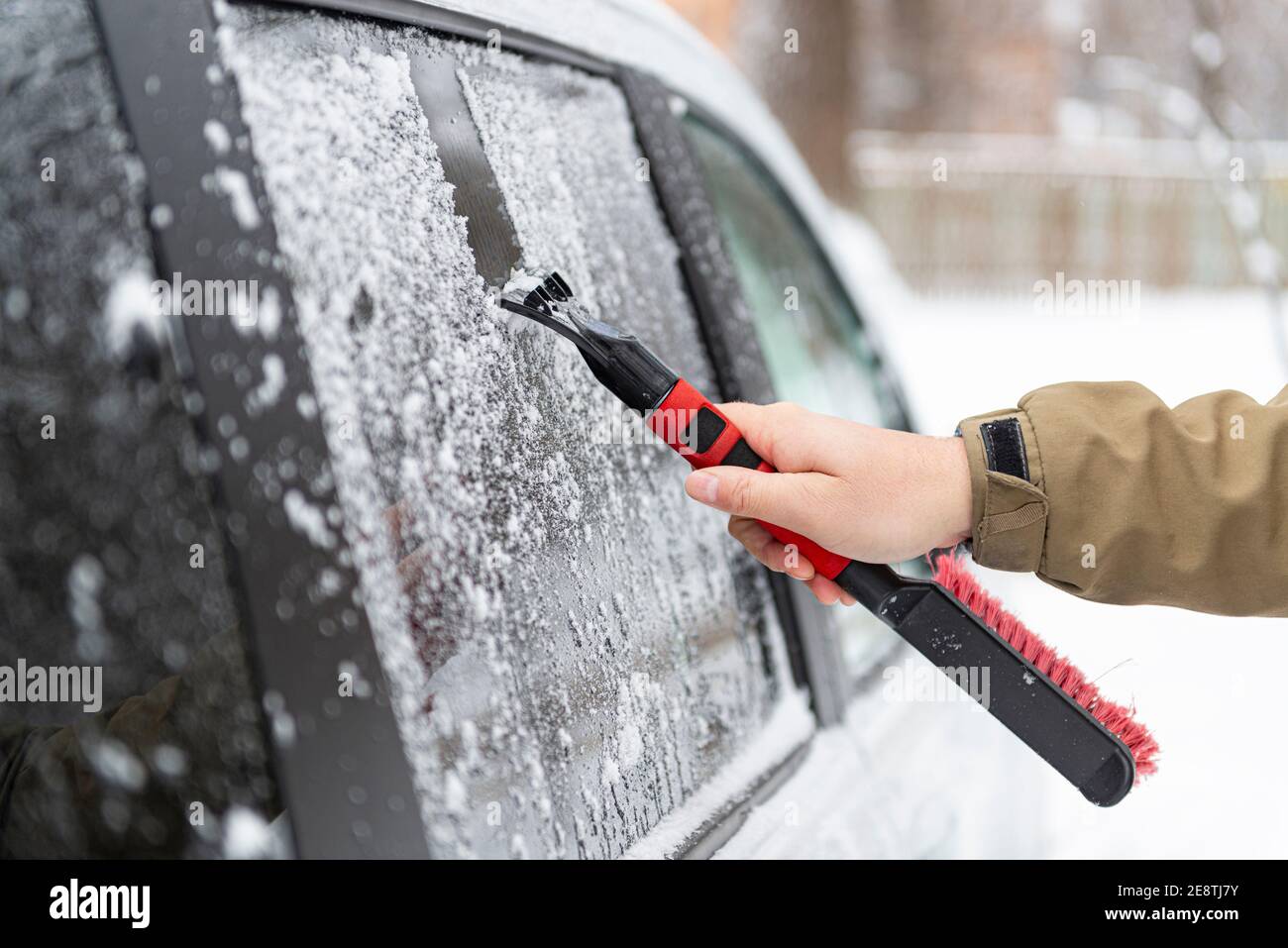 Autofahrer Hand mit Bürste oder Schaber entfernt Schnee und Eis aus dem Autoglas nach starkem Schneefall. Schlechte Wettervorhersage für das Fahren. Sicherheit auf der Straße c Stockfoto