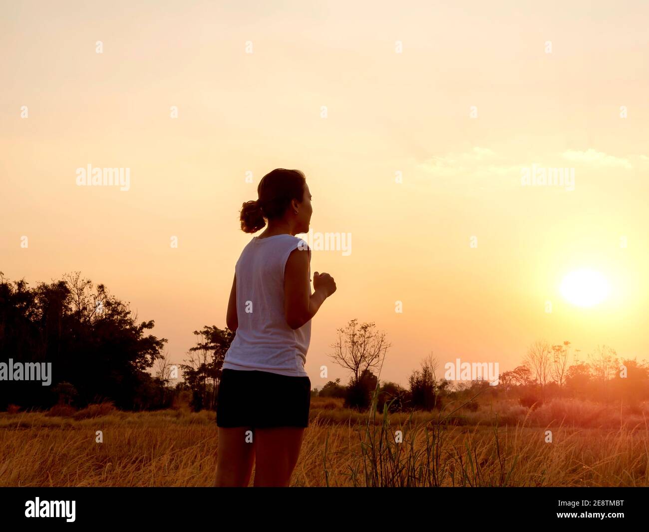 Junge Frau läuft auf ländlichen Betonstraße auf schönen hellen Sonnenuntergang Himmel Hintergrund in der Nähe des Sommerfeldes. Lifestyle Abend Lauf Hintergrund. Fitness und Stockfoto