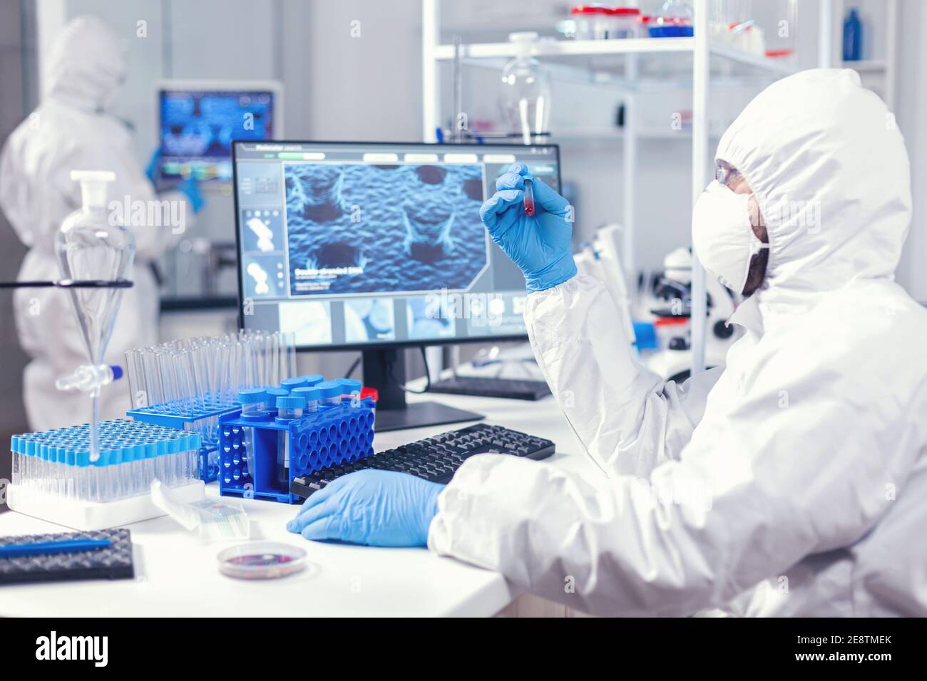 Wissenschaftler in Schutzanzug hält Probe von infiziertem Blut mit Coronavirus in Reagenzglas. Arzt arbeitet mit verschiedenen Bakterien und Gewebe, pharmazeutische Forschung für Antibiotika gegen Covid19. Stockfoto