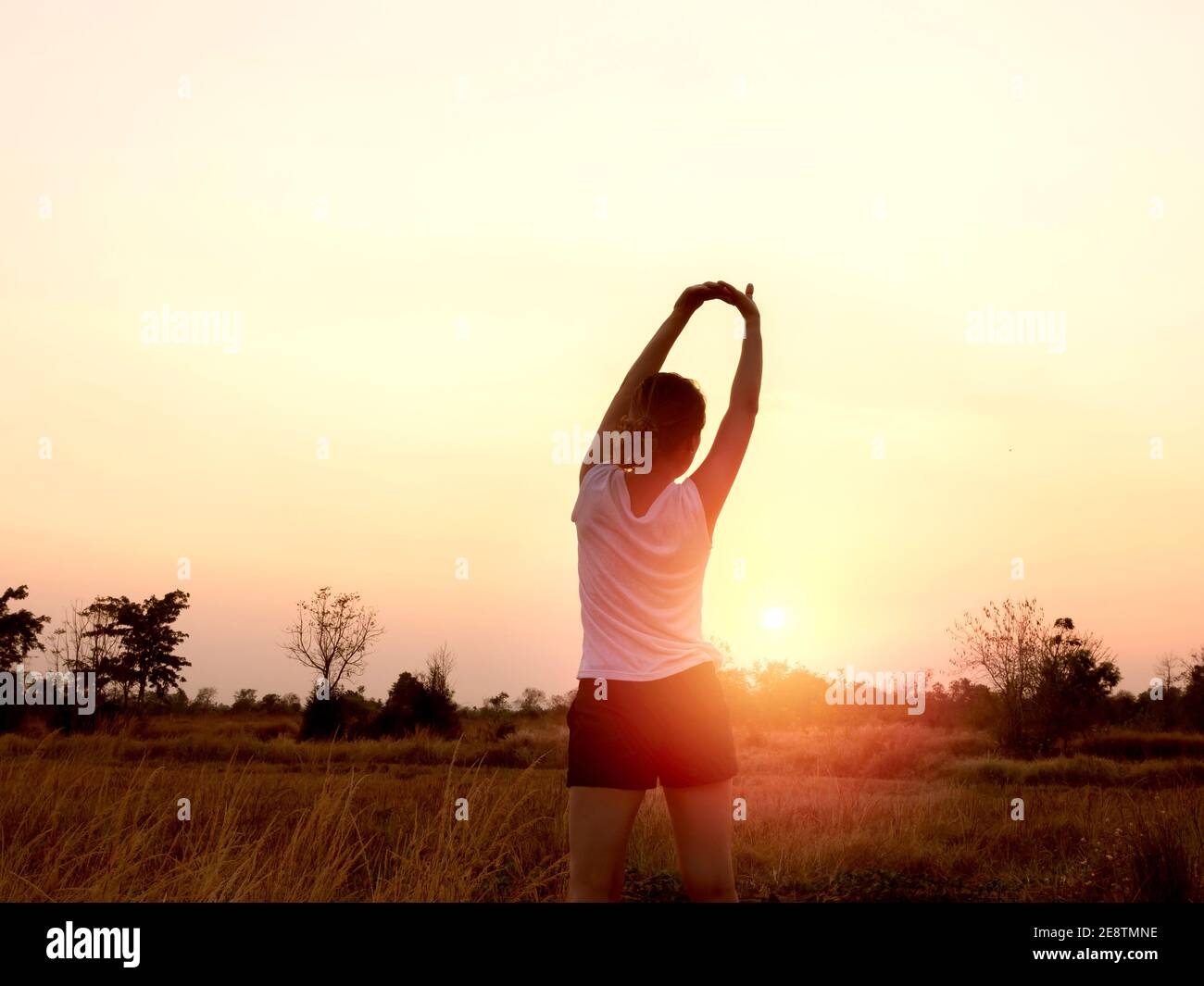 Junge Frau streckt ihre Arme auf schönen hellen Sonnenuntergang Himmel Hintergrund in der Nähe des Sommerfeldes. Zurück der weiblichen Erwärmung im Freien vor dem Training. Fitne Stockfoto