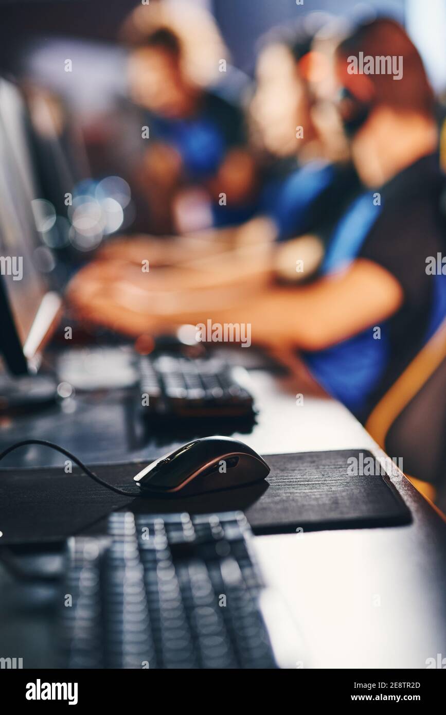 ESports Turnierkonzept. Nahaufnahme eines professionellen Cyber-Sportlers am Arbeitsplatz mit Desktop-Computer, Tastatur und Maus, selektiver Fokus. Gruppe von Spielern im Hintergrund Stockfoto