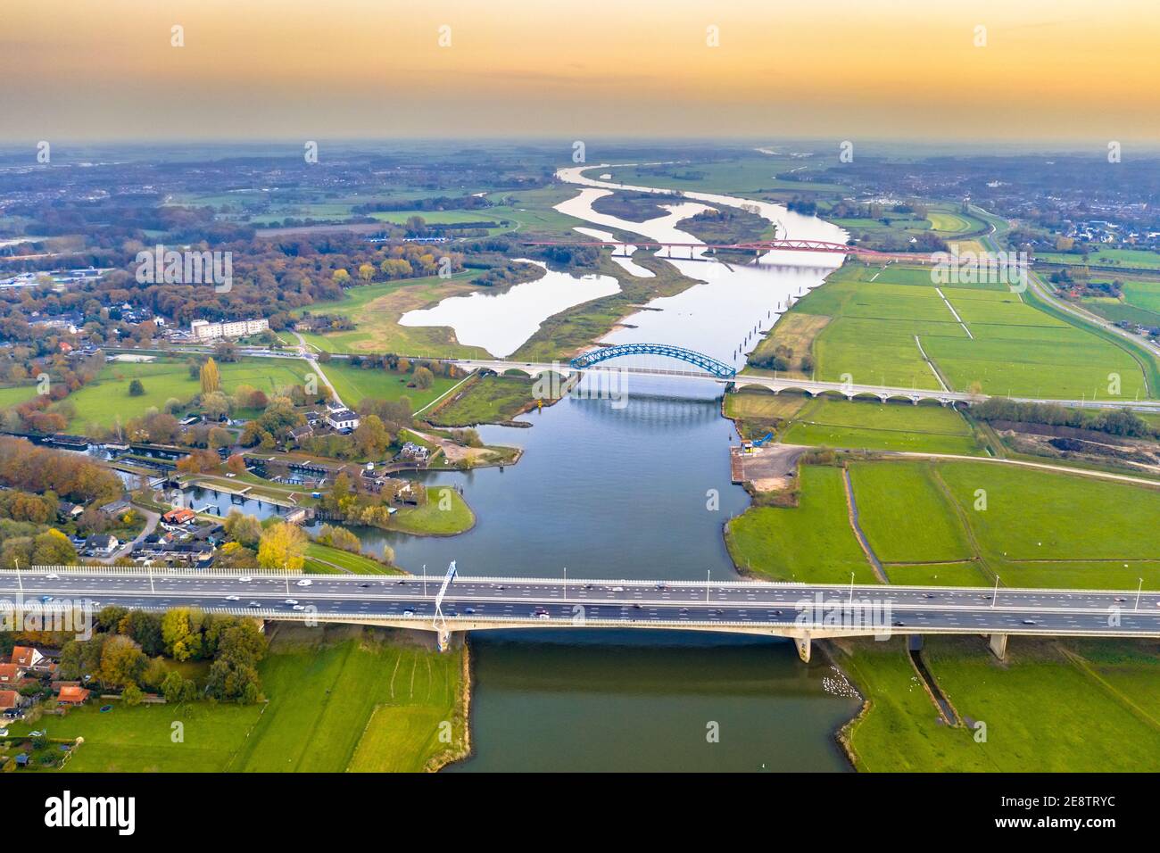 Luftaufnahme des riesigen Tieflandflusses IJssel mit Autobahn und Eisenbahnbrücken durch Sonnenuntergangslandschaft. Zwolle, Overijssel Provinz, Niederlande. Dro Stockfoto
