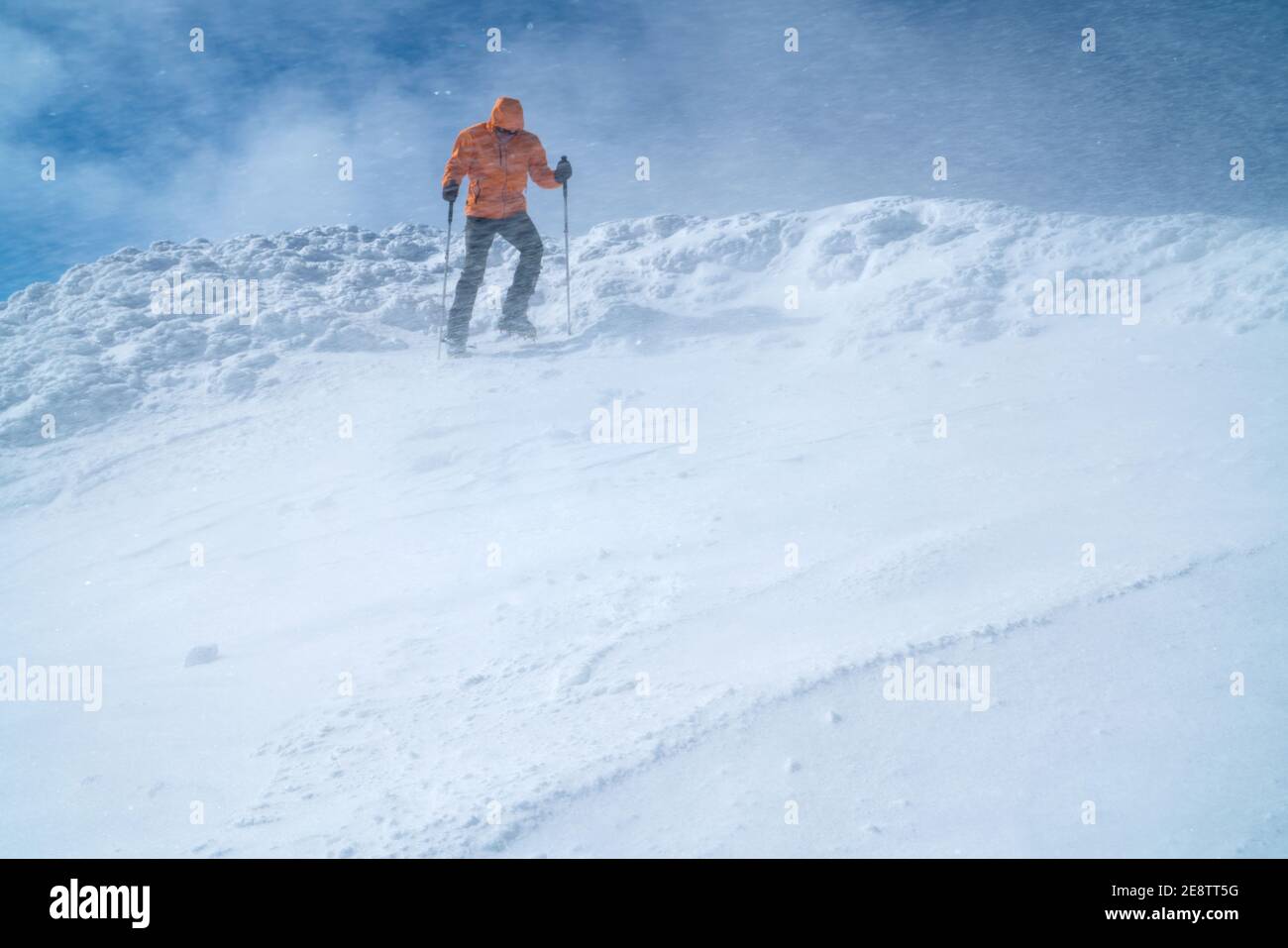 Hochbergsteiger gekleidet leuchtend orange Softshell Jacke mit einem Trekking-Stöcke Abstieg der schneebedeckten Berggipfel. Konzept für aktive Menschen auf Ve Stockfoto