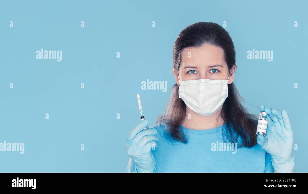 Ärztin mittleren Alters in medizinischer Maske und Handschuhen mit Covid-19 Coronavirus-Impfstoff und Spritze. Konzept der erfolgreichen Impfentwicklung und Beginn der Immunisierung Stockfoto
