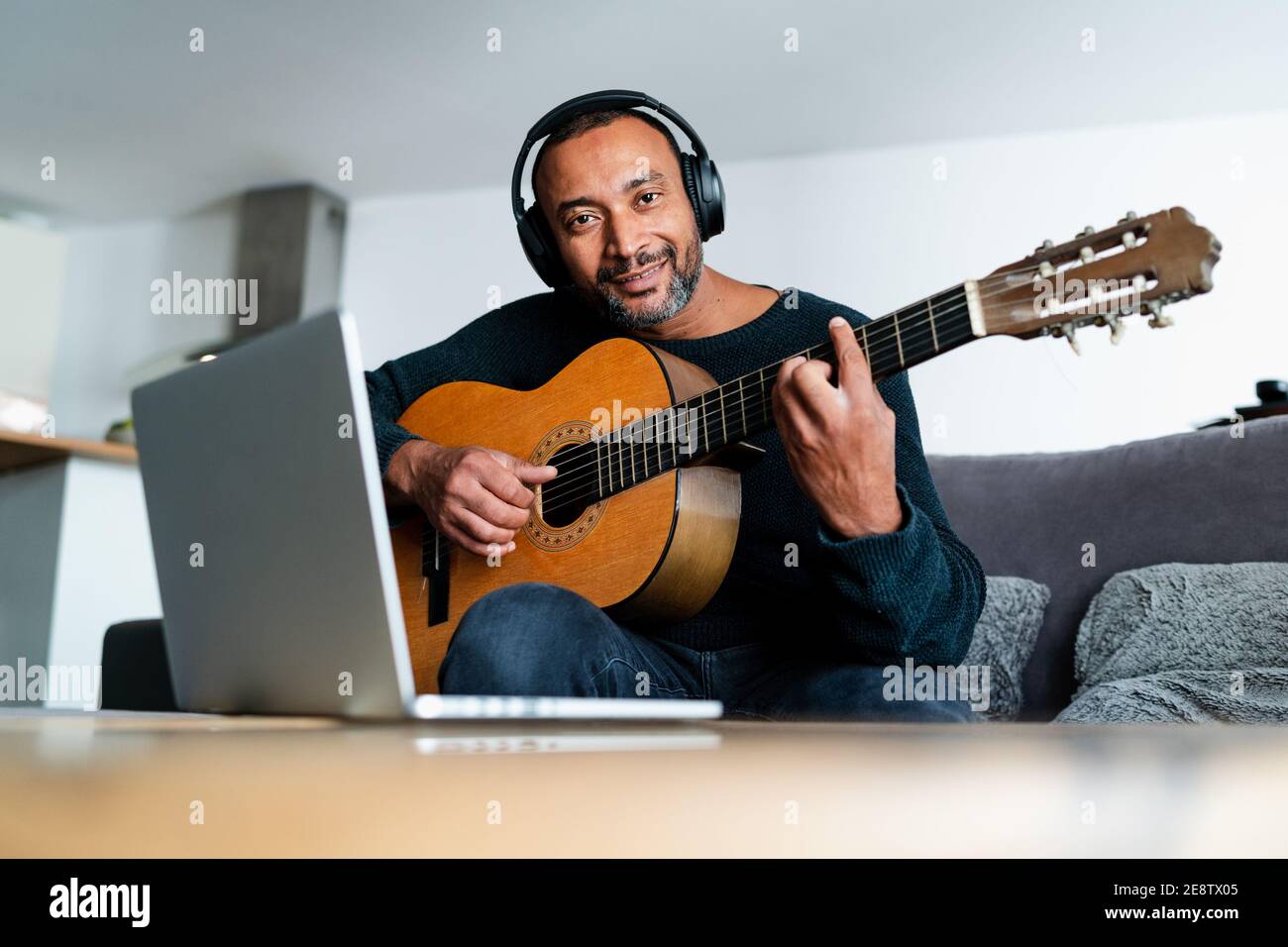 40 Jahre alter Mann spielt Gitarre zu Hause und Mit einem Laptop Stockfoto