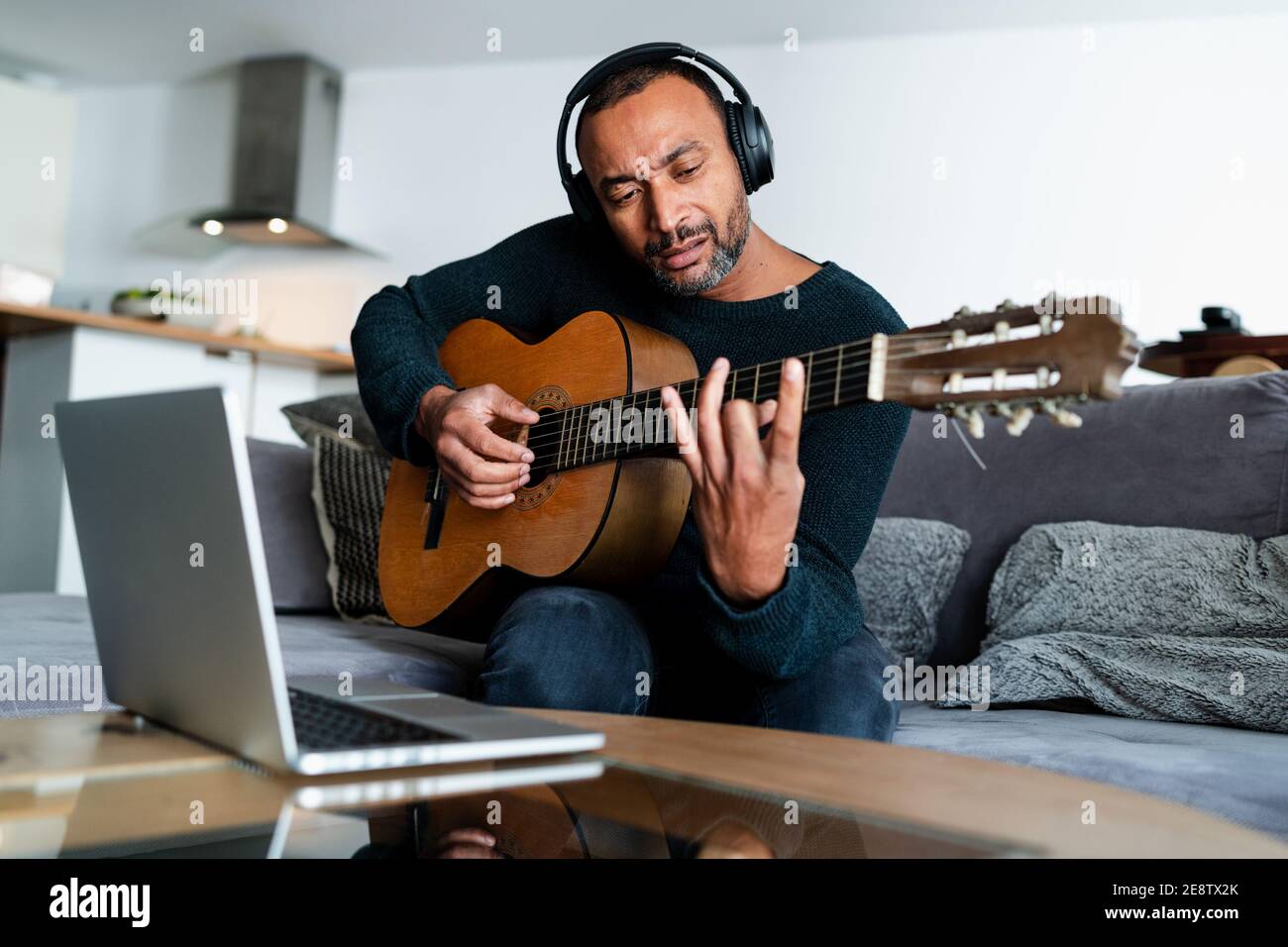 Entspannter Mann spielt die Gitarre zu Hause und mit einem Notebook Stockfoto