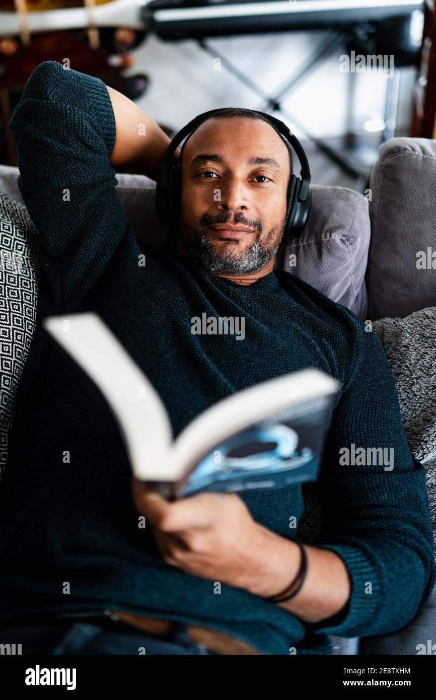 Gemischter Rennmensch auf dem Sofa zu Hause und Lesen eines Buches Stockfoto