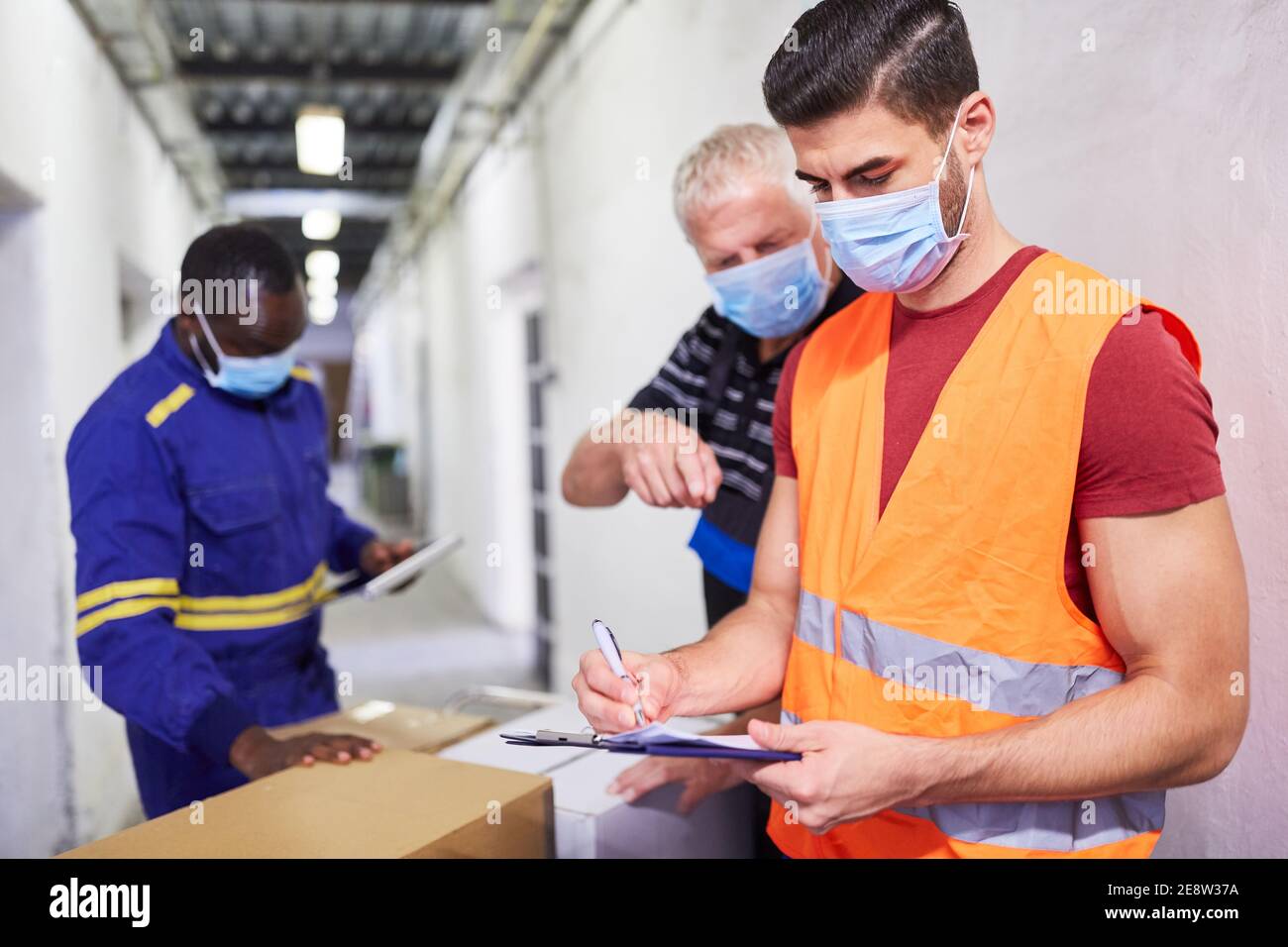 Drei Arbeiter mit Gesichtsmasken wegen Covid-19 am Wareneingang mit Checkliste Stockfoto