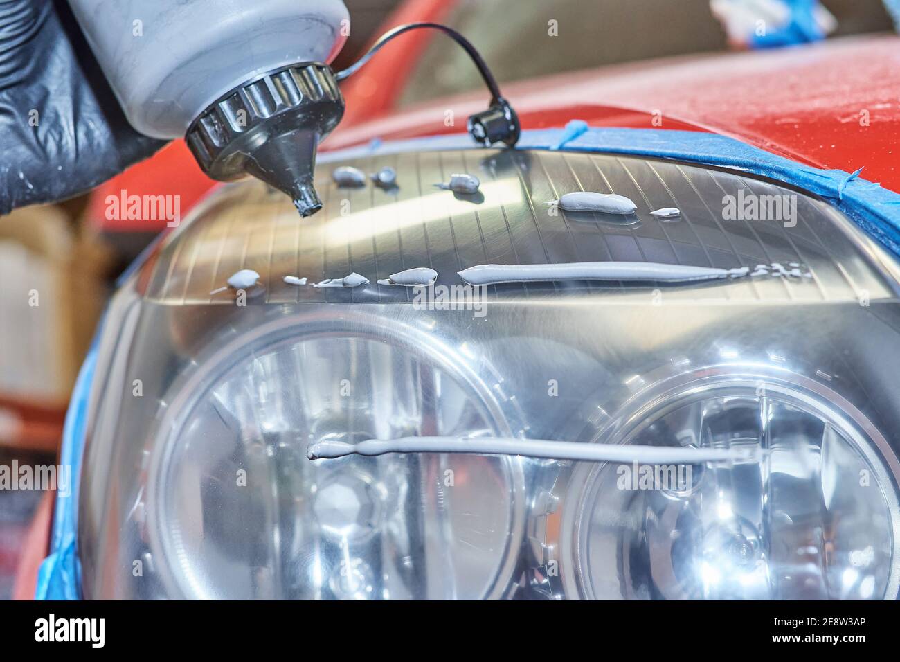 Die Hand des Mechanikers mit dem Handschuh, der ein spezielles anwendet Produkt zum Polieren und Wiederherstellen der Scheinwerfer eines Autos Stockfoto