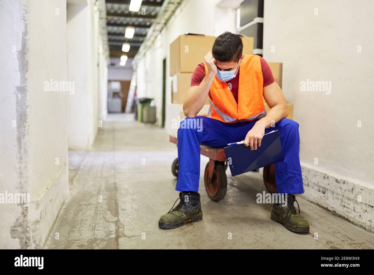 Gestresster und erschöpfter Arbeiter mit Gesichtsmaske wegen Covid-19 Im Lager Stockfoto