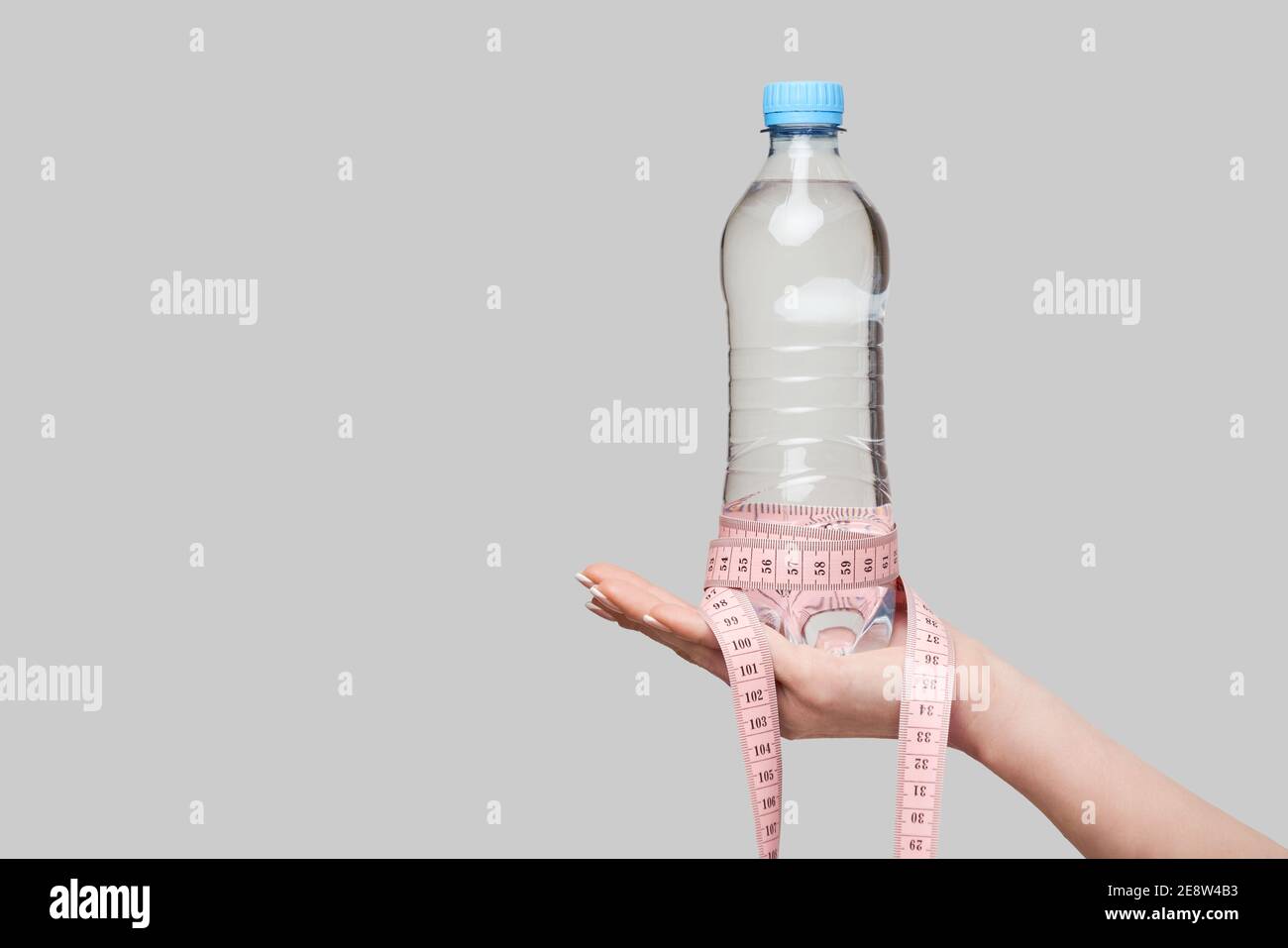 Weight Loss Diet Konzept - eine Flasche Trinkwasser und Maßband in menschlicher Hand isoliert auf grauem Hintergrund Stockfoto