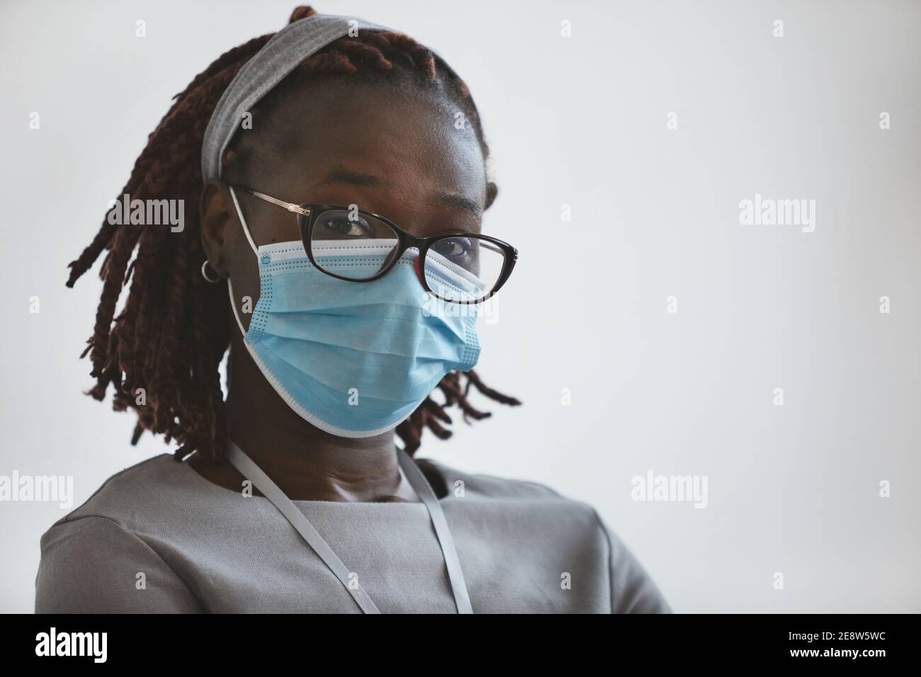 Kopf- und Schulterporträt einer jungen afroamerikanischen Frau, die Maske und Brille trägt, während sie vor weißem Hintergrund steht und auf die Kamera schaut, Co Stockfoto