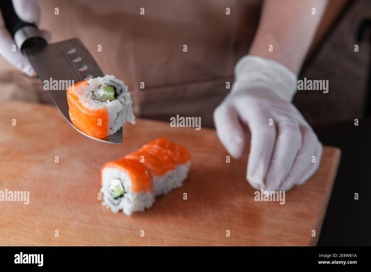 Cook schneidet Sushi und hält ein Stück auf der Klinge Eines Messers Stockfoto