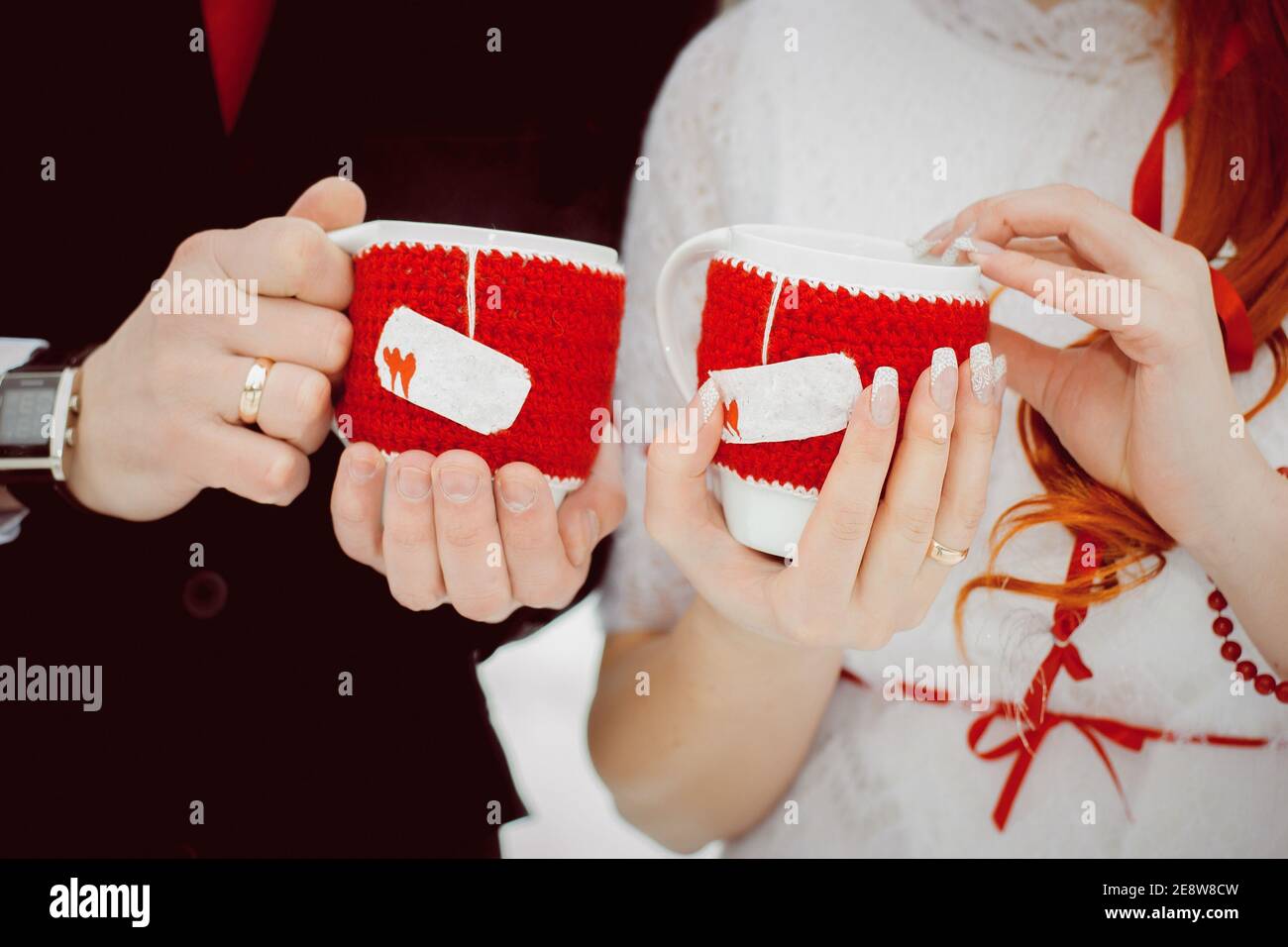 Tassen in gestrickten roten Bezügen mit Herzen mit heißem Tee Und Dampf in den Händen der Liebhaber Stockfoto