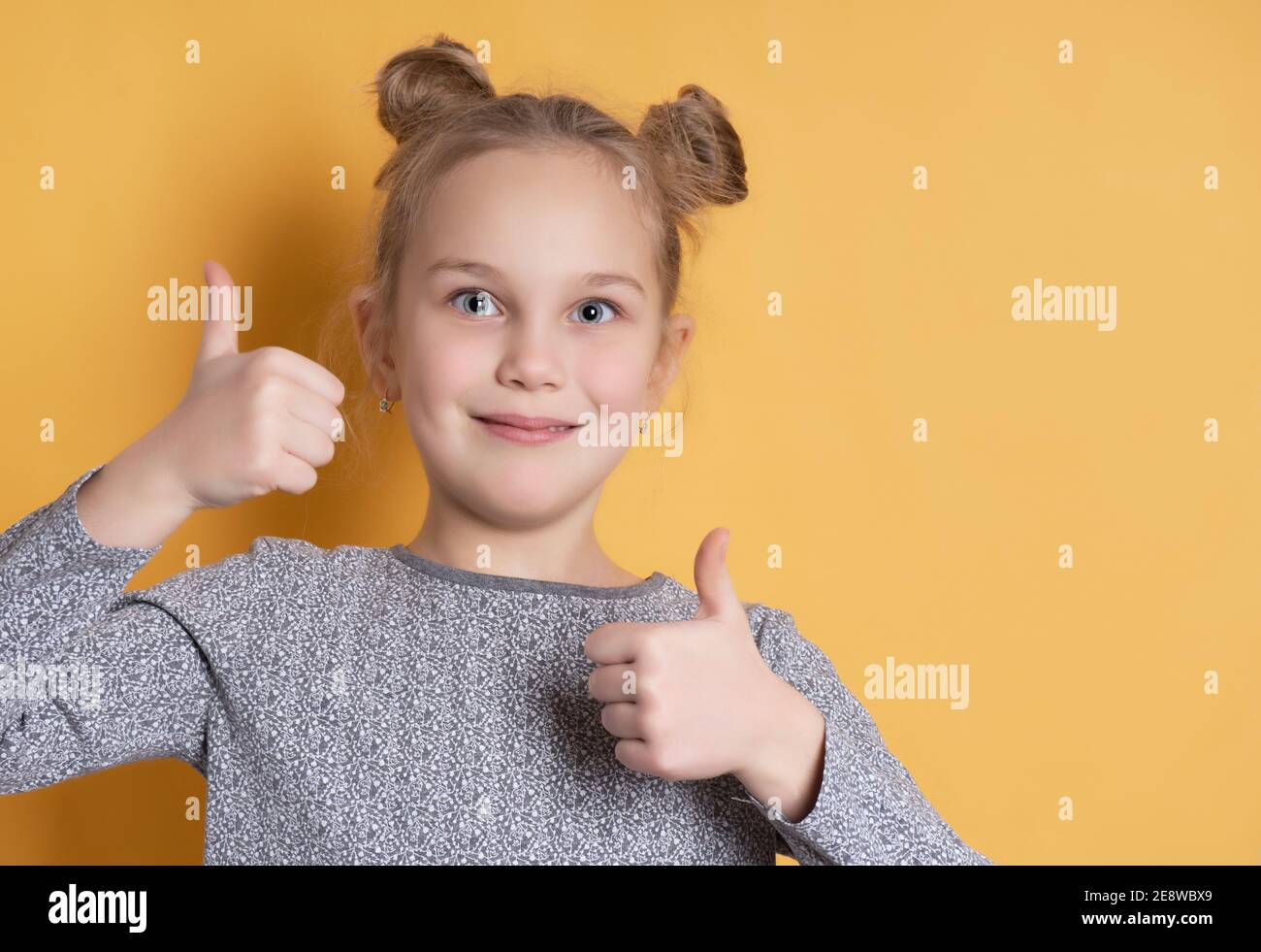 Portrait von niedlichen kleinen Mädchen lächelnd zahnlos und zeigt Daumen nach oben auf gelbem Hintergrund. Nahaufnahme Gesicht eines Mädchens mit einer fröhlichen Frisur. Die Konz Stockfoto