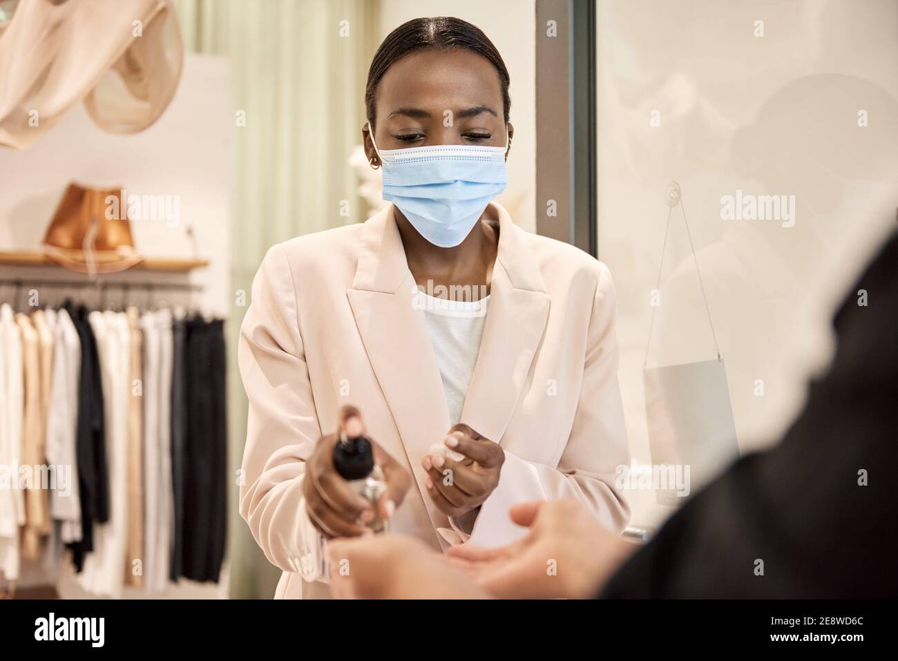 Afroamerikanischer Boutique-Besitzer, der einem Kunden Desinfektionsmittel in die Hände gibt Stockfoto