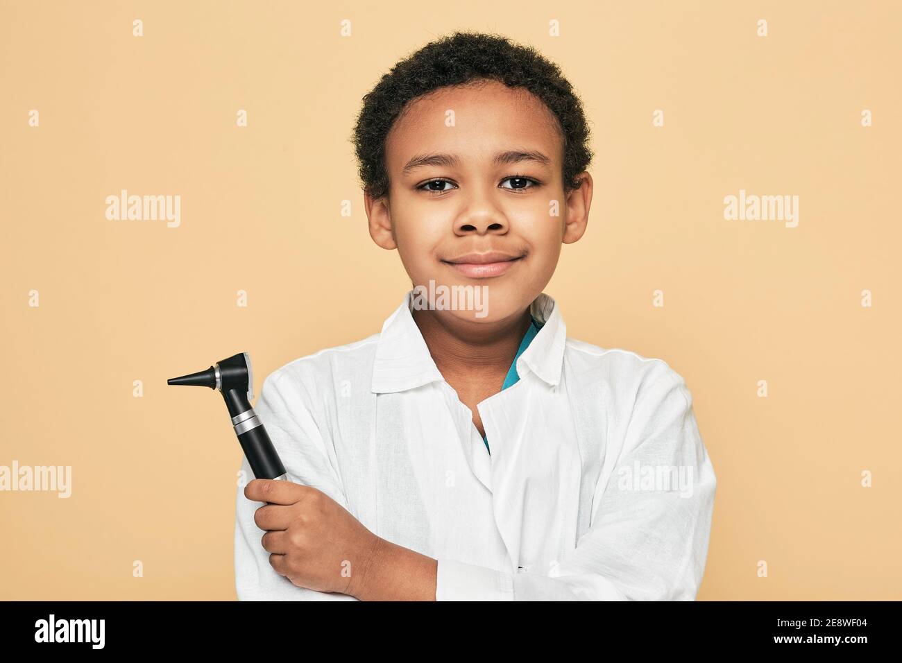 Afroamerikanischer Junge mit Otoskop auf beigem Hintergrund. Ohrbehandlung und Hörtest für Kinder Stockfoto