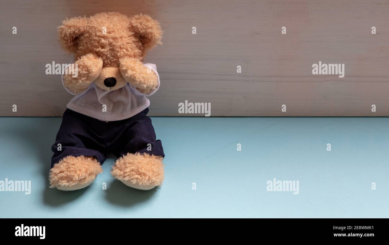 Kindesmissbrauch, häusliche Gewalt Konzept. Teddybär sitzt allein auf blauem Boden in einem leeren Kinderzimmer und bedeckt die Augen, Stockfoto