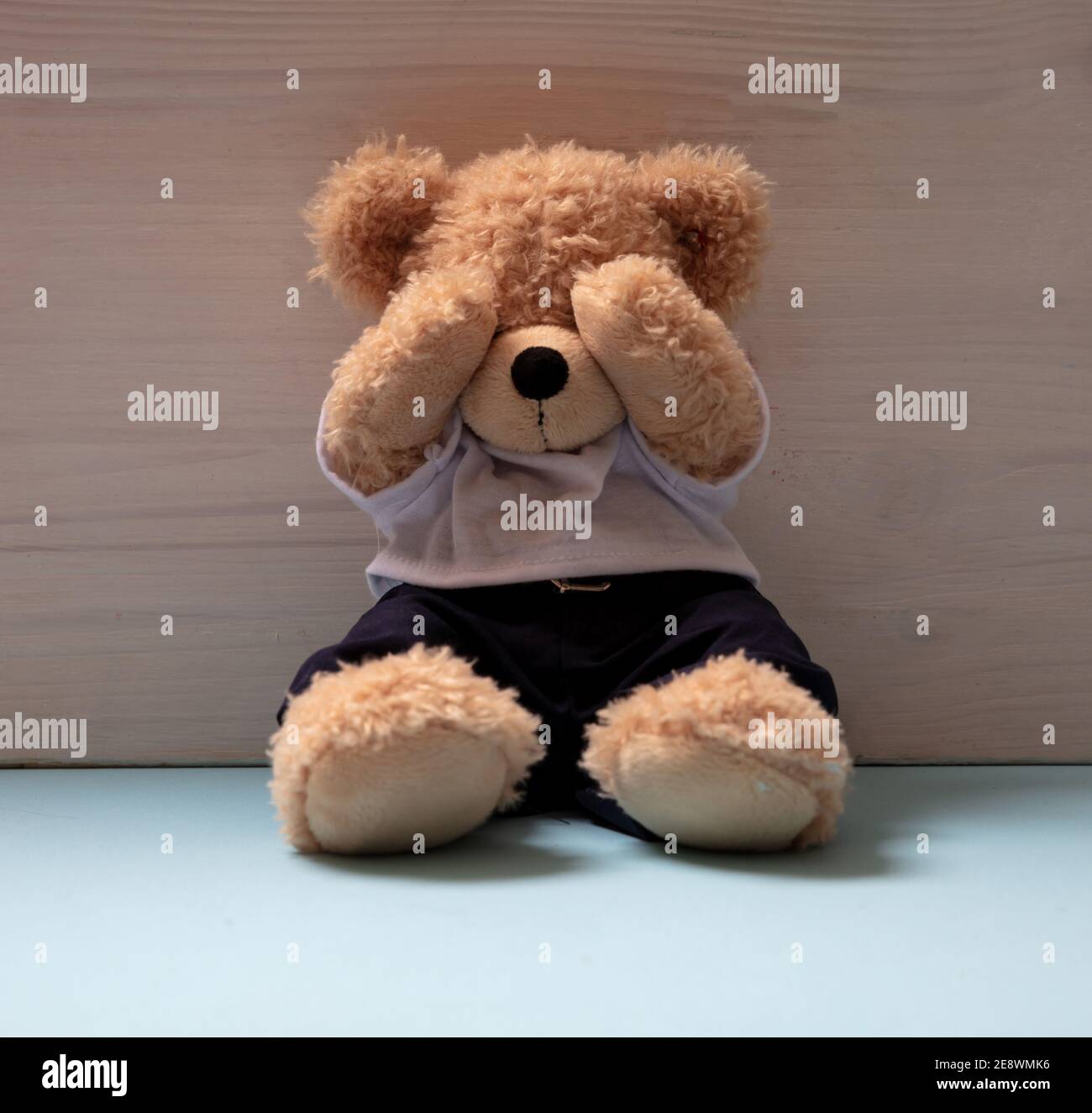 Teddybär sitzt allein auf blauem Boden in einem leeren Kinderzimmer, Augen bedeckt, Kindesmissbrauch, traurige Angst Kind Konzept. Stockfoto