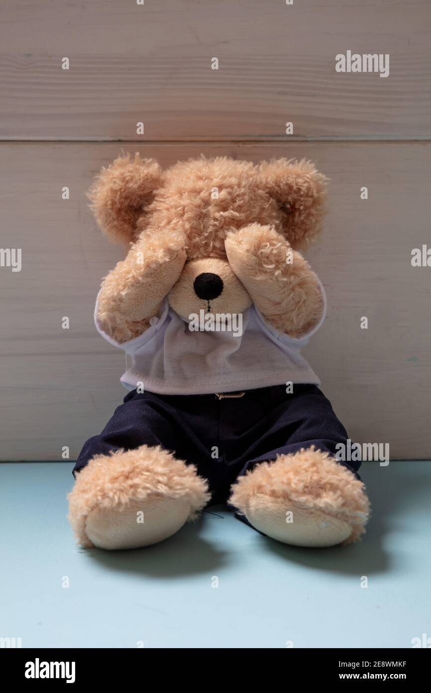 Kindesmissbrauch, häusliche Gewalt Konzept. Teddybär sitzt allein auf blauem Boden in einem leeren Kinderzimmer und bedeckt die Augen, Stockfoto