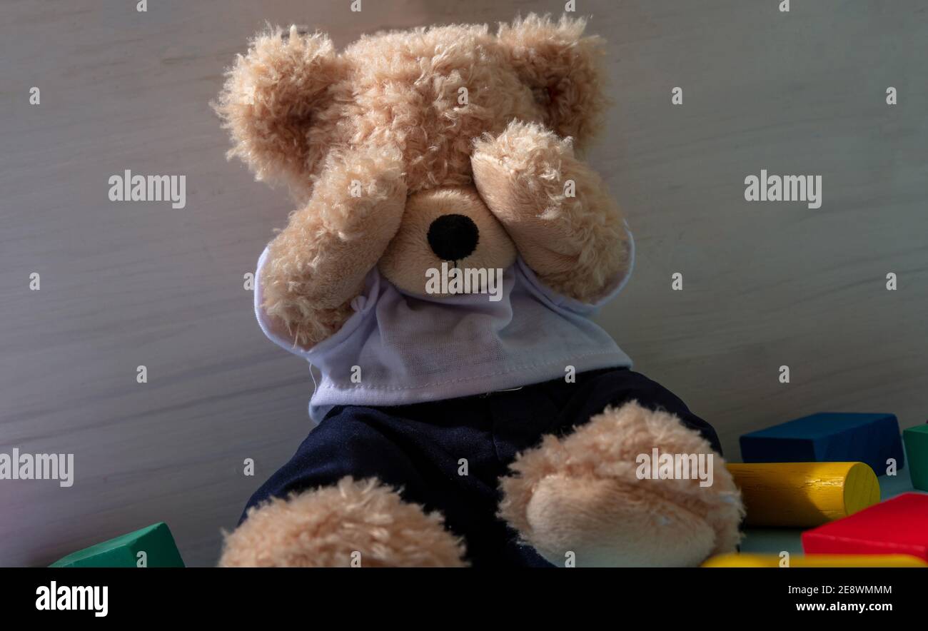 Konzept für Kindesmissbrauch. Teddybär bedeckt die Augen, sitzt auf dem Boden des Kinderzimmers, bunte Holzblöcke herum Stockfoto