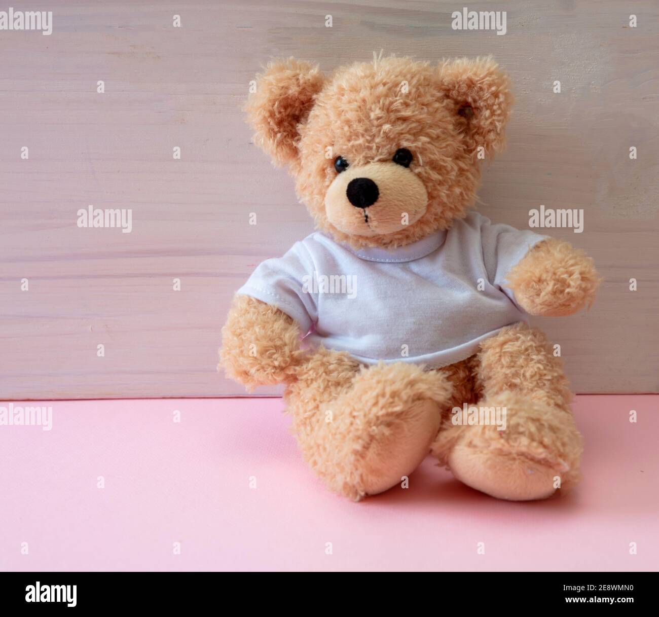 Teddy-Mädchen sitzt in einem leeren Raum, pastellrosa Farbe Boden, weiß Holz Wand Hintergrund, Kind allein im Kinderzimmer Konzept Stockfoto