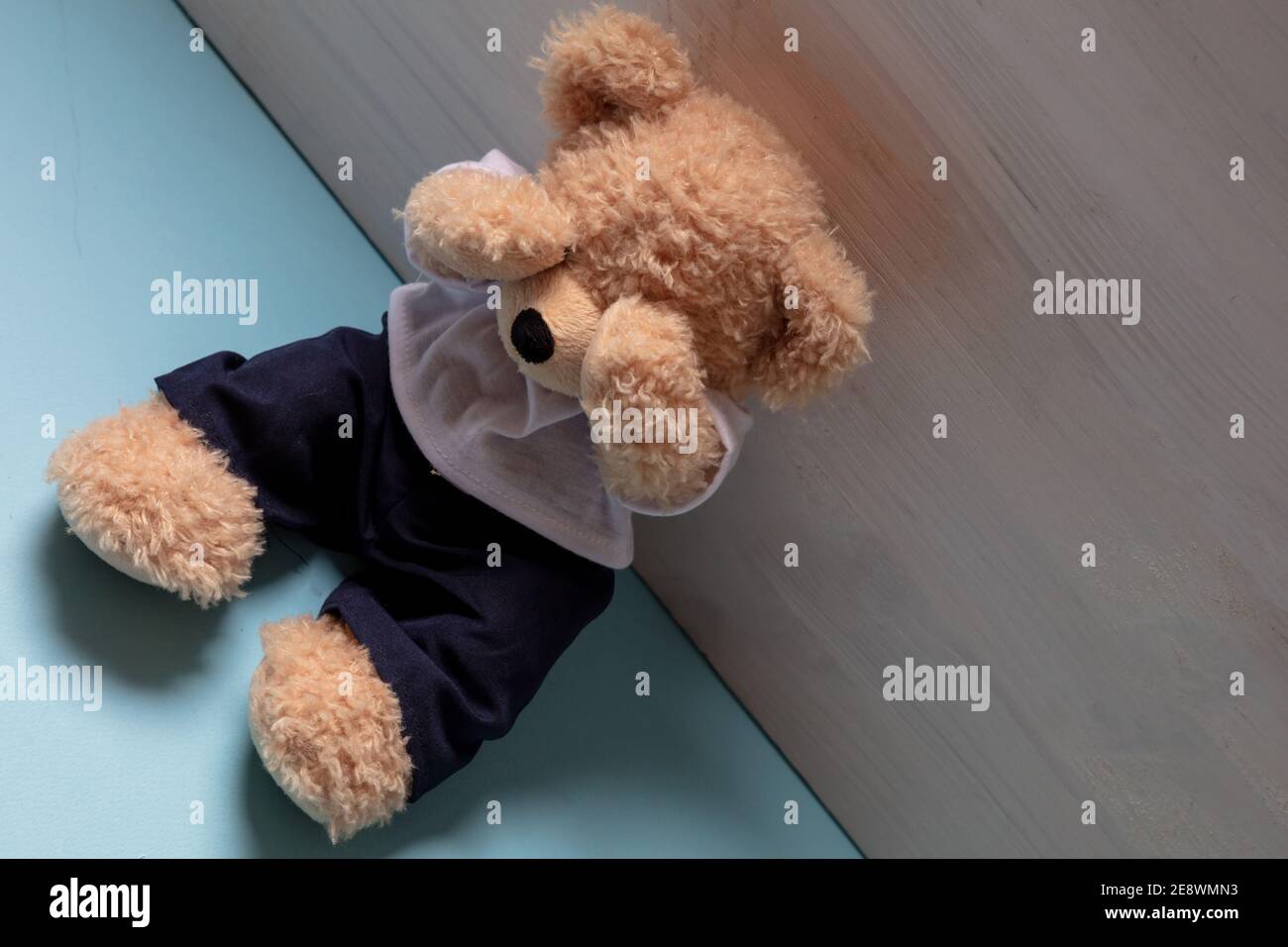 Teddybär sitzt allein auf blauem Boden in einem leeren Kinderzimmer, Augen bedeckt, Kindesmissbrauch, traurige Angst Kind Konzept. Stockfoto