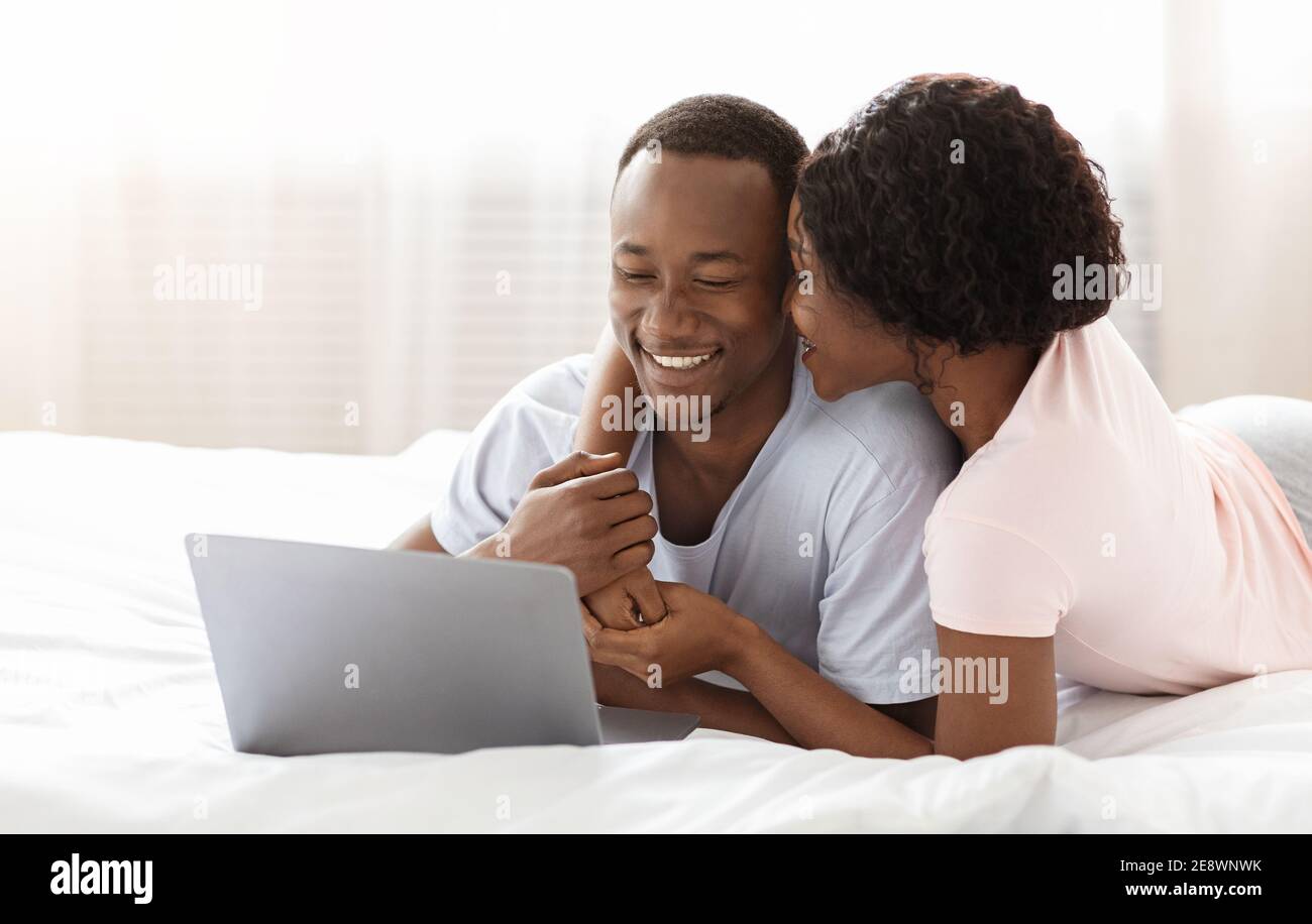 Romantischer schwarzer Mann und Frau mit Laptop im Bett Stockfoto