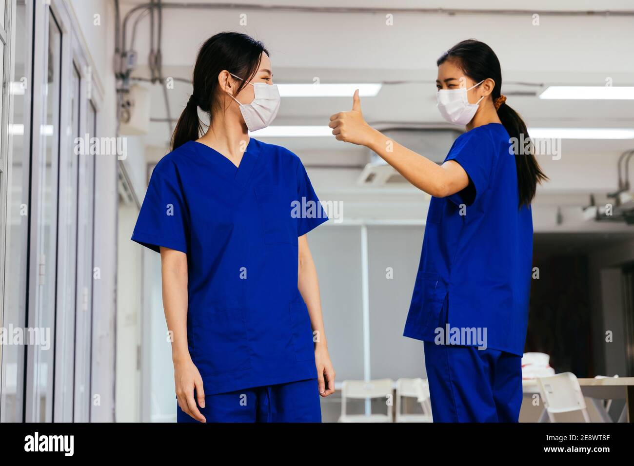Junge schöne asiatische Krankenschwester in Peeling Uniform trägt Gesichtsmaske bewundern und geben Daumen bis zu Mitarbeiter im Krankenhaus während Covid19 Pandemie. Vertrauen und gute Zusammenarbeit im Konzept der Unternehmenskultur Stockfoto
