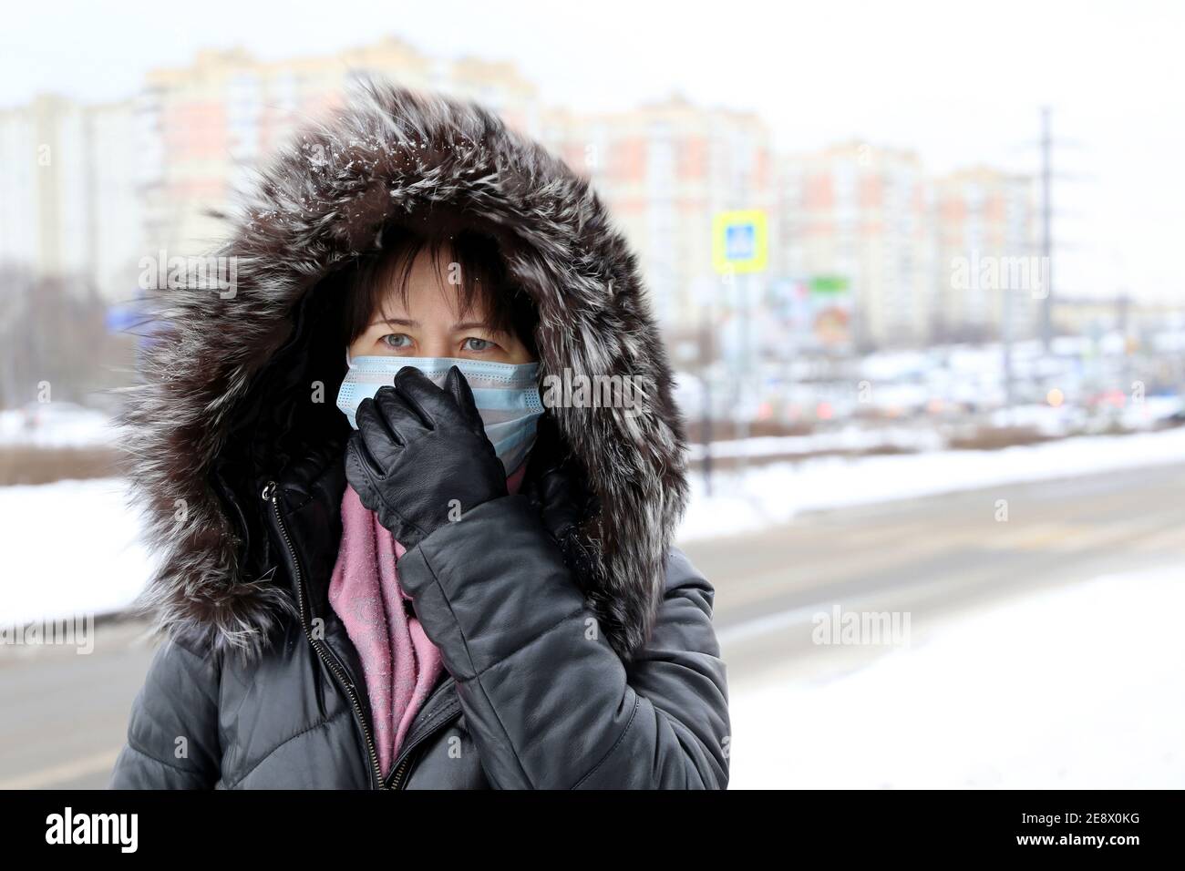 Coronavirus-Schutz, Frau in medizinischer Maske und Pelzhaube auf Winterstraße während des Schnees stehend. Konzept von Krankheit, Fieber, Erkältung und Grippe Stockfoto
