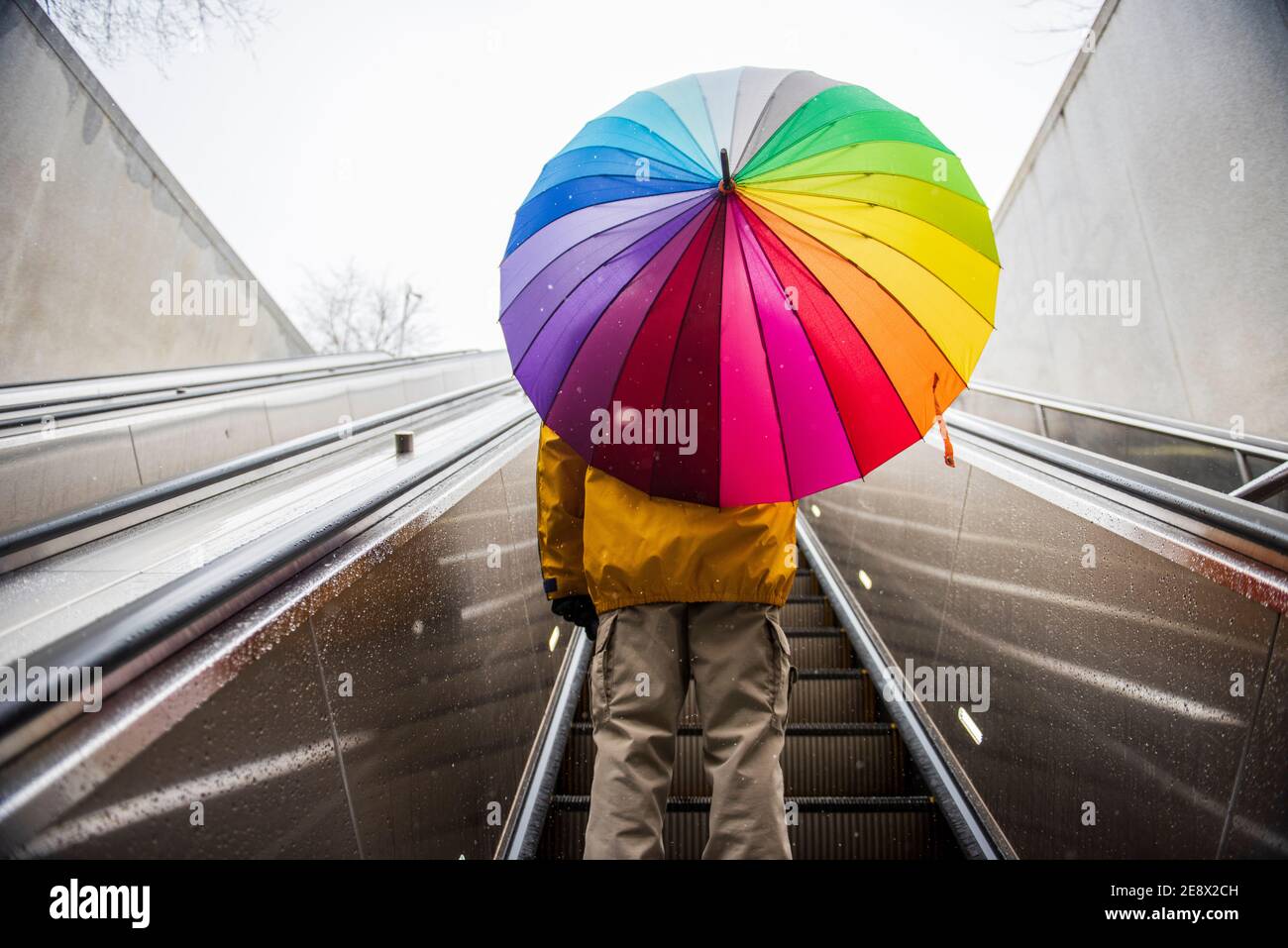 Ein Mann, der einen Regenbogenschirm trägt, fährt mit der Metro-Rolltreppe in Washington, D.C. Stockfoto