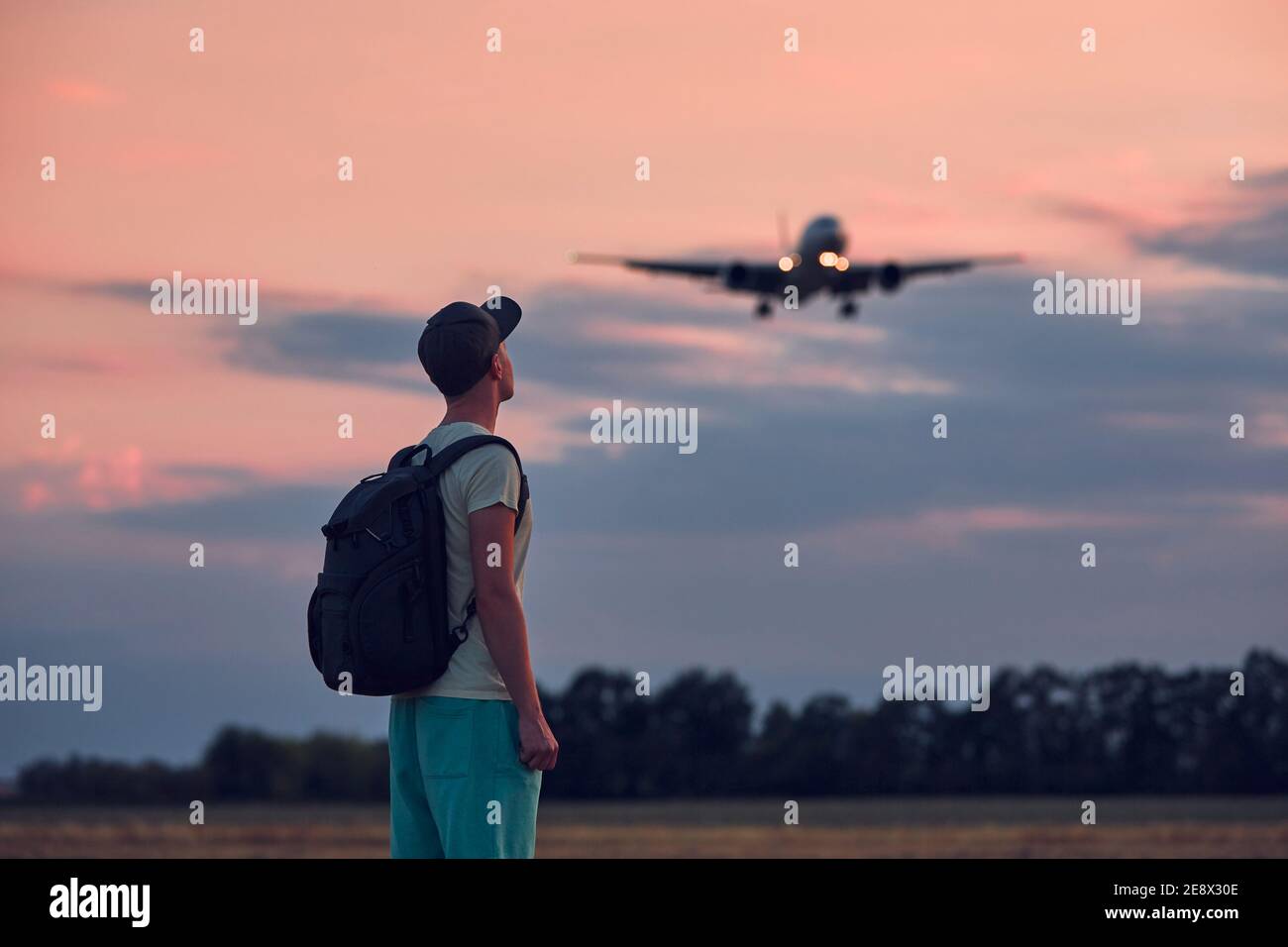 Junger Mann, der in der Dämmerung auf ein fliegendes Flugzeug gegen den launischen Himmel blickt. Themen Nostalgie für Reisen und Luftfahrt. Stockfoto