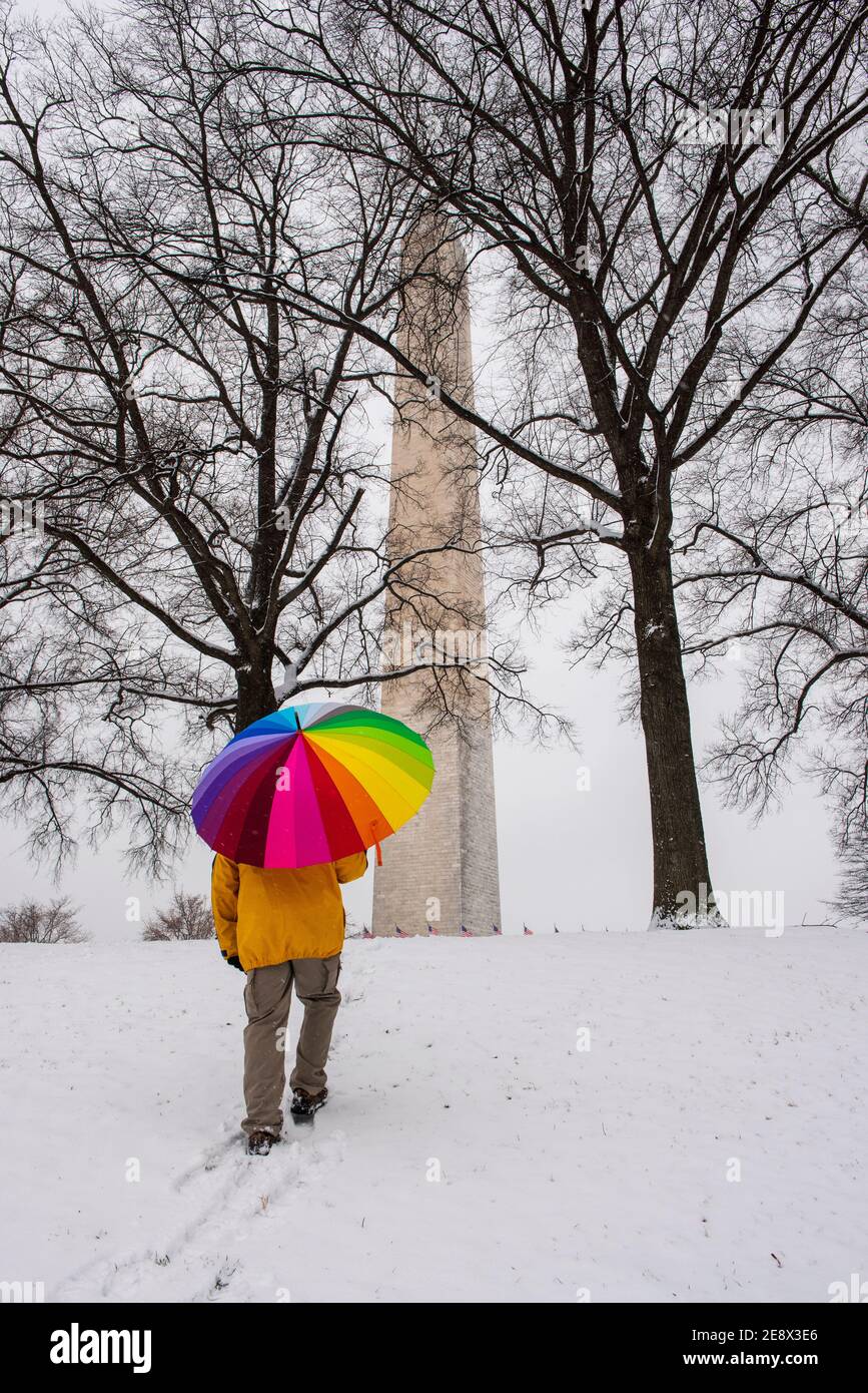 Ein Mann mit einem bunten Regenschirm geht während eines verschneiten Tages in der National Mall in Washington, D.C. zum Washignton Monument Stockfoto