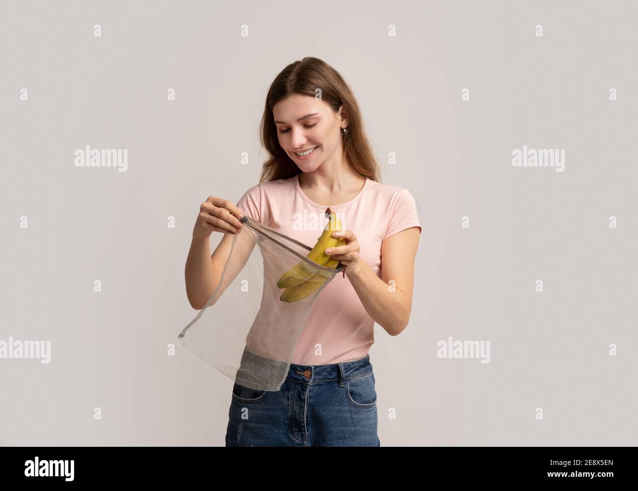 Null Verschwendung Einkaufen. Happy Millennial Woman Putting Bananen In Wiederverwendbare String-Tasche Stockfoto