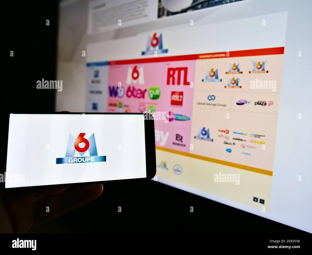 Person, die ein Mobiltelefon mit dem Logo der französischen Medienholding Metropole Télévision S.A. (Groupe M6) auf dem Display hält. Fokus auf Handy-Bildschirm. Stockfoto